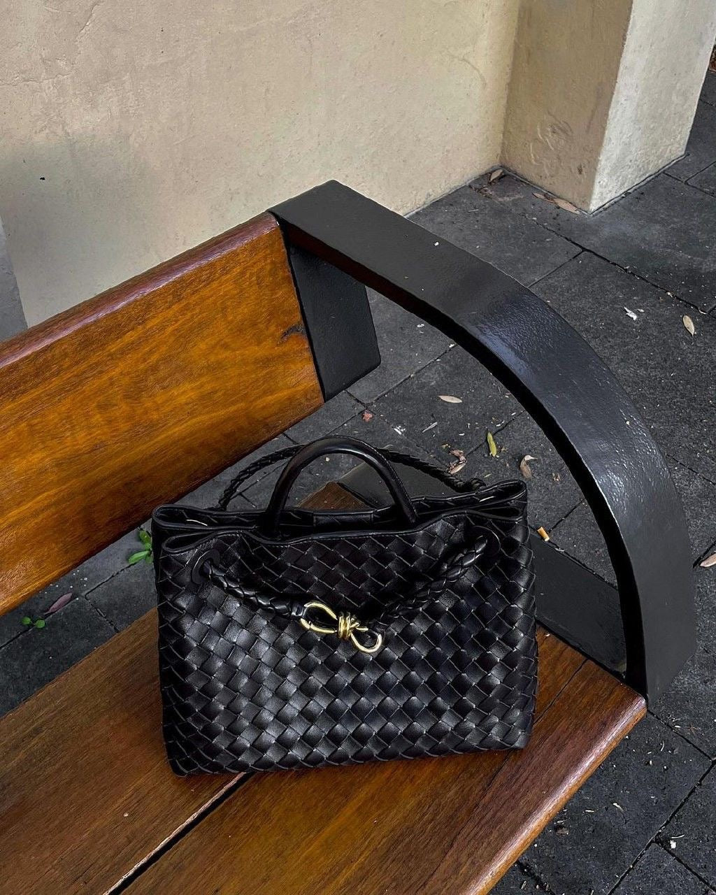 Black woven handbag on a wooden bench with a concrete floor background