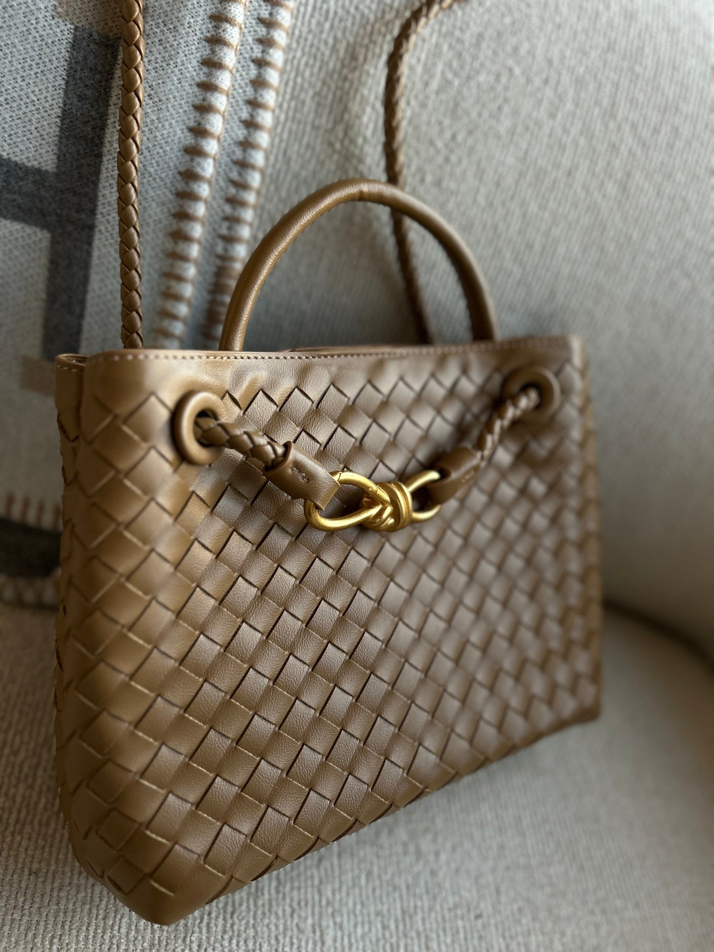 Brown woven handbag with a gold clasp on a textured surface
