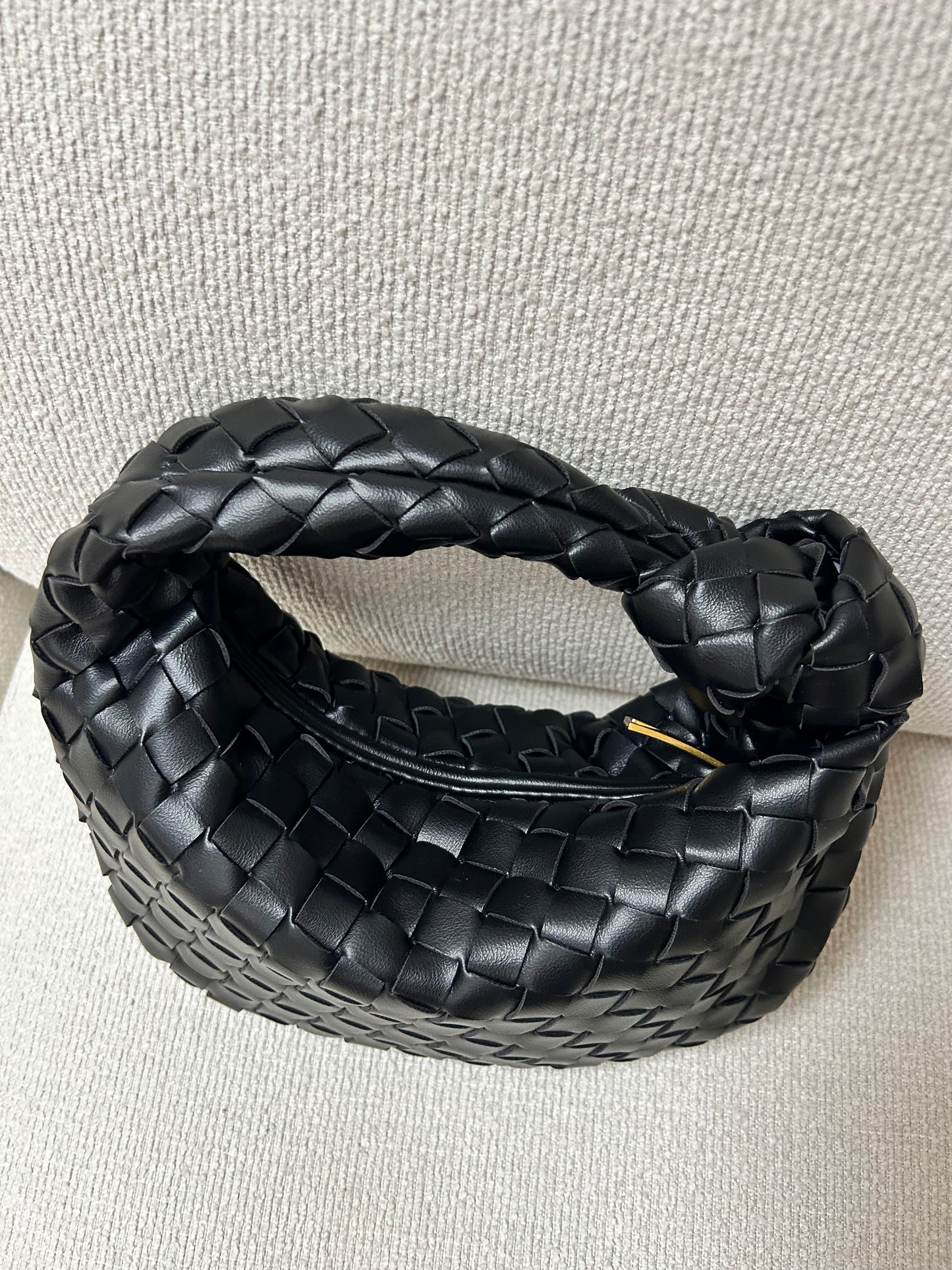 Elegant black woven clutch bag placed on a neutral coloured couch