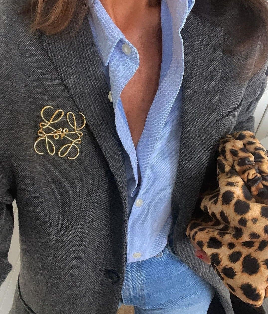 Person wearing a gray blazer with a gold old money brooch, light blue shirt, and leopard print sleeve.