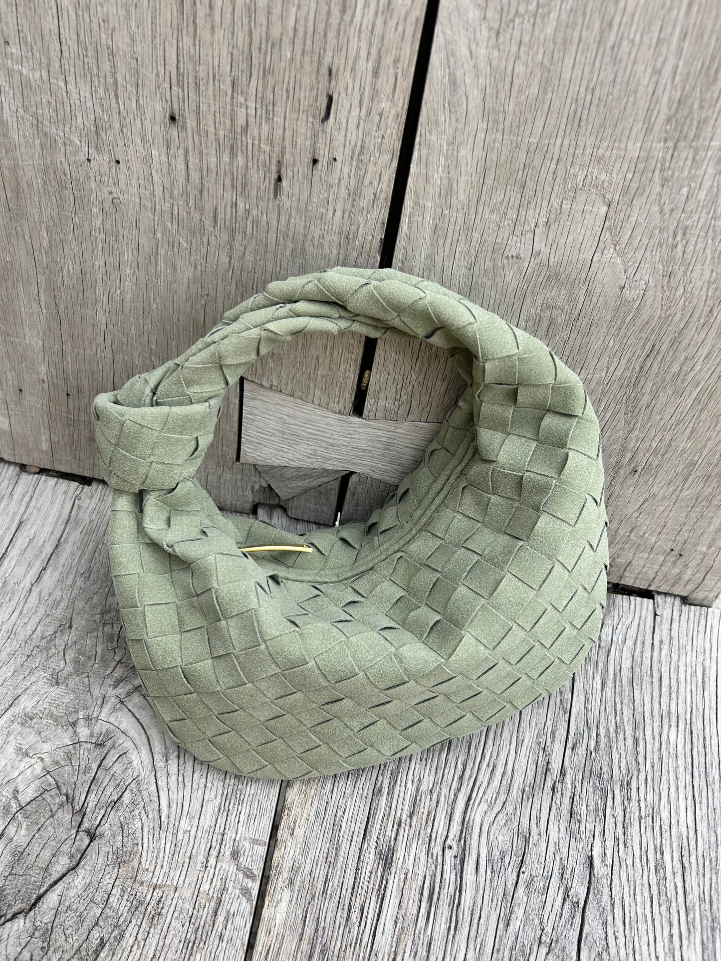 small sage green woven clutch placed on a wooden bench