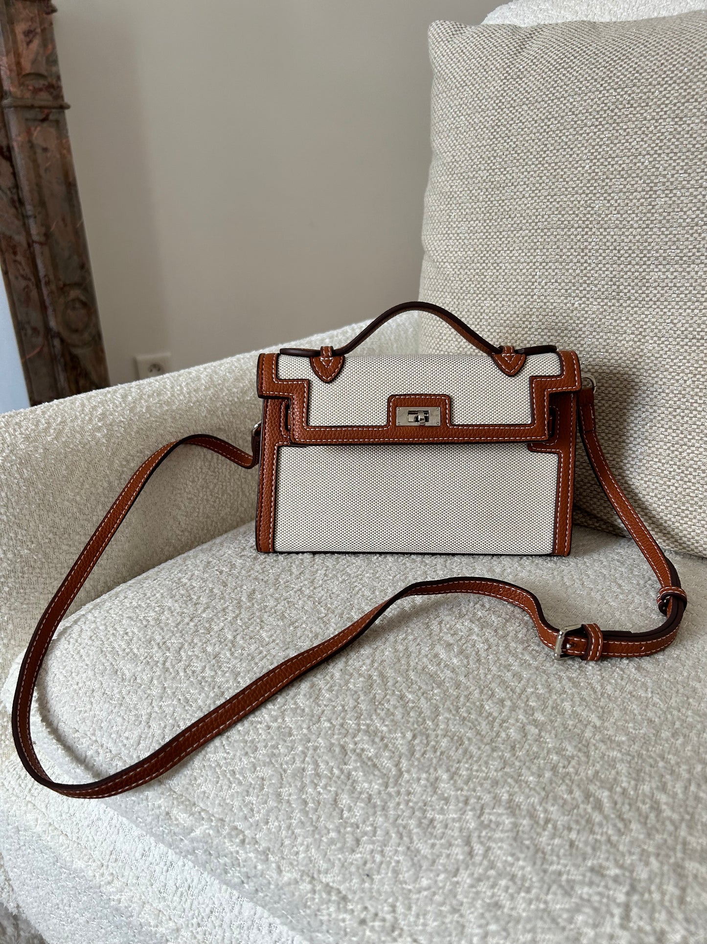 Crafted from premium textured canvas with bold black leather-look trim and contrast stitching, this beauty means business. The silver-tone hardware and unique dual-strap illusion detail add a high-fashion edge, while the structured silhouette screams polished perfection. Whether you're heading to a coffee meeting or jet-setting to your next luxury escape, this bag always delivers main-character energy.