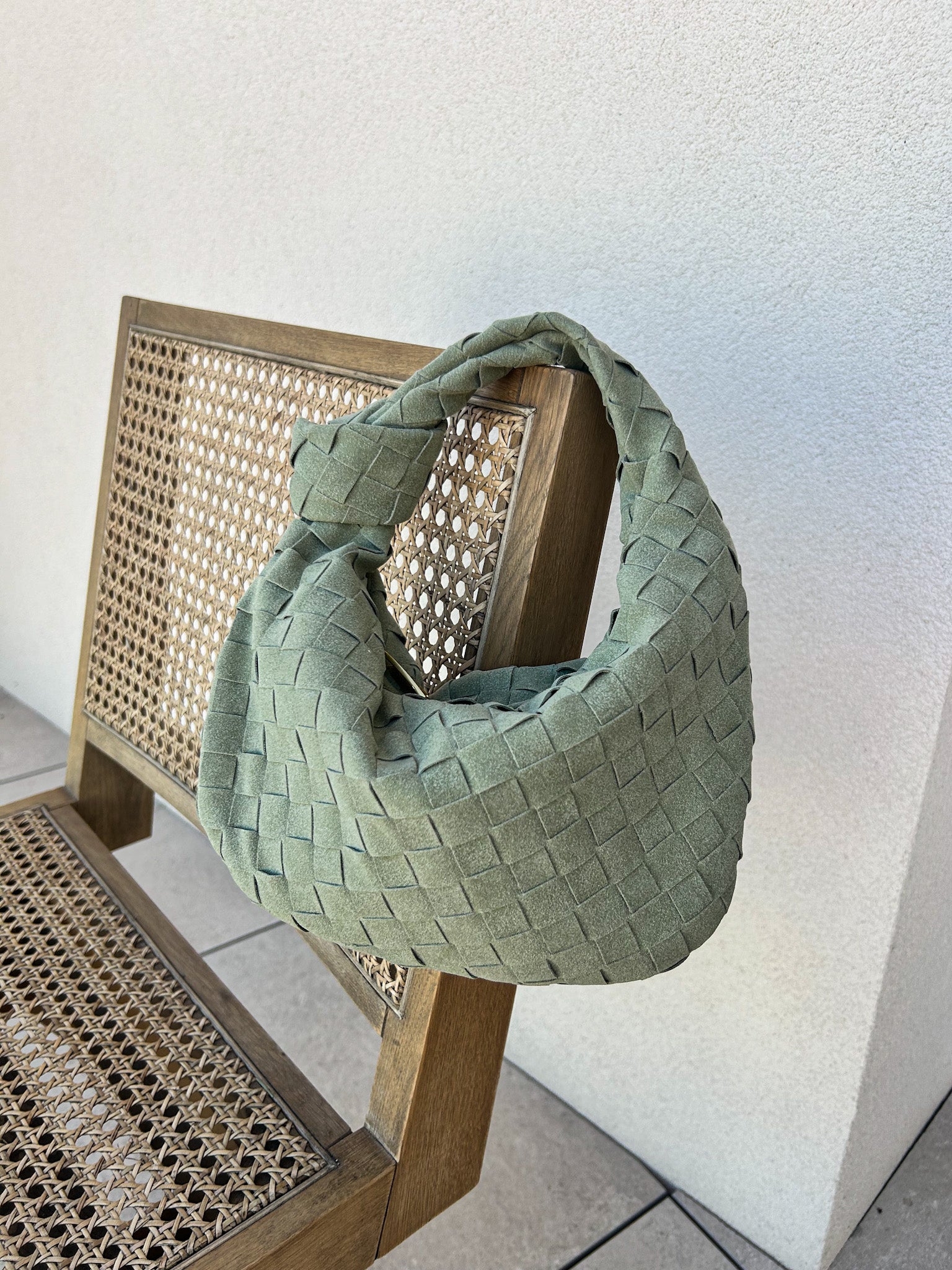 A green woven clutch handbag made of vegan suede material, displayed on a wooden chair.