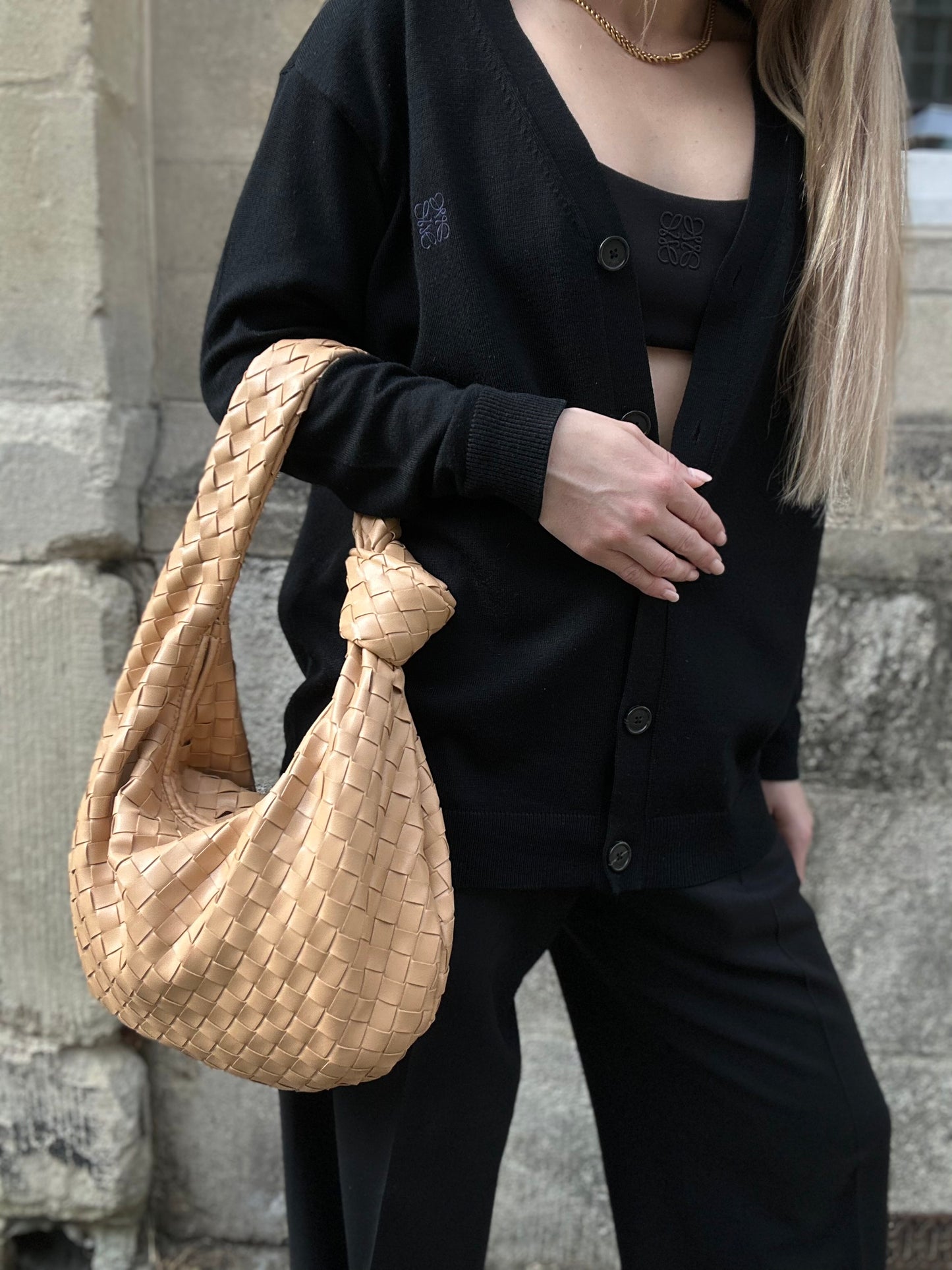 A person holding a beige, woven medium handbag with a retro woven design.