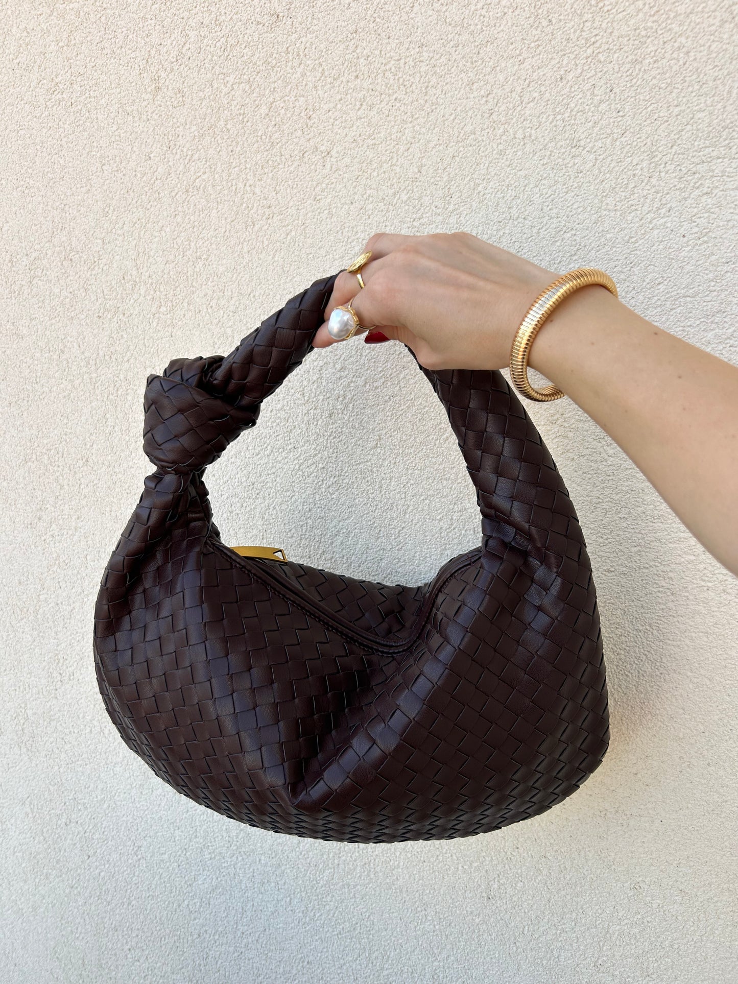 A person's hand holding a brown woven dumpling-shaped shoulder handbag.