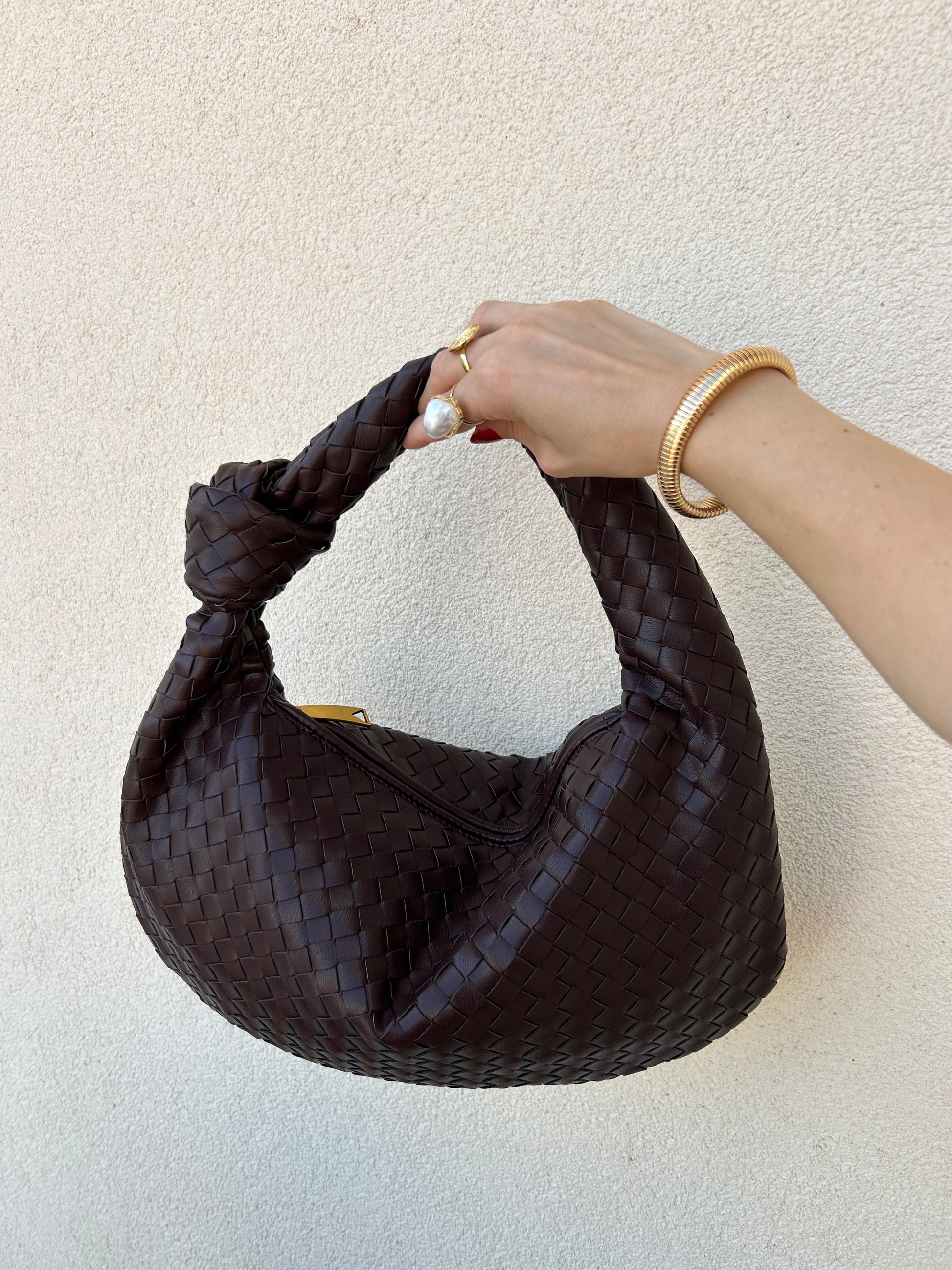 A person's hand holding a brown woven dumpling-shaped shoulder handbag.