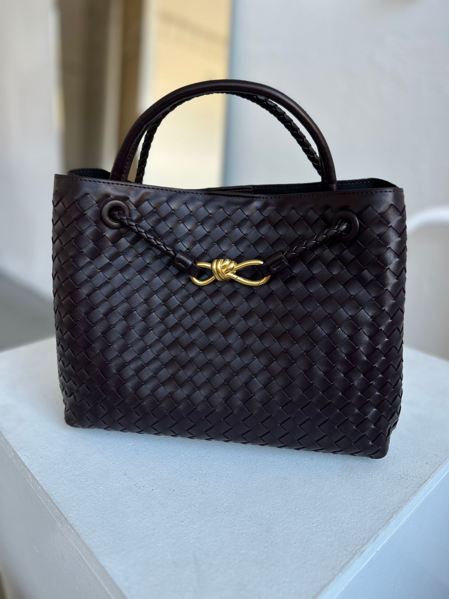 A structured dark-chocolate woven handbag crafted from premium vegan leather, featuring elegant gold detailing and spacious interior design — the perfect everyday-meets-luxury piece for stylish women.