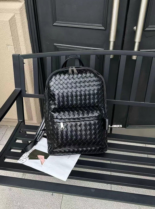 Black woven textured backpack on a black metal bench with a door in the background. Black woven cowhide leather unisex backpack with minimalist luxury design perfect for work, travel and everyday use.
