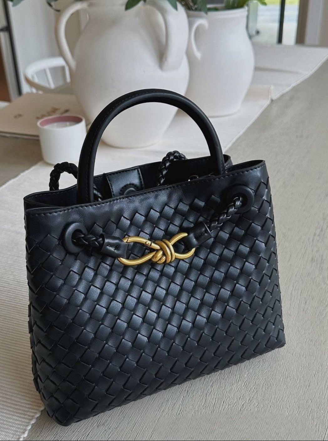 Black woven handbag with gold clasp  detail on a light surface