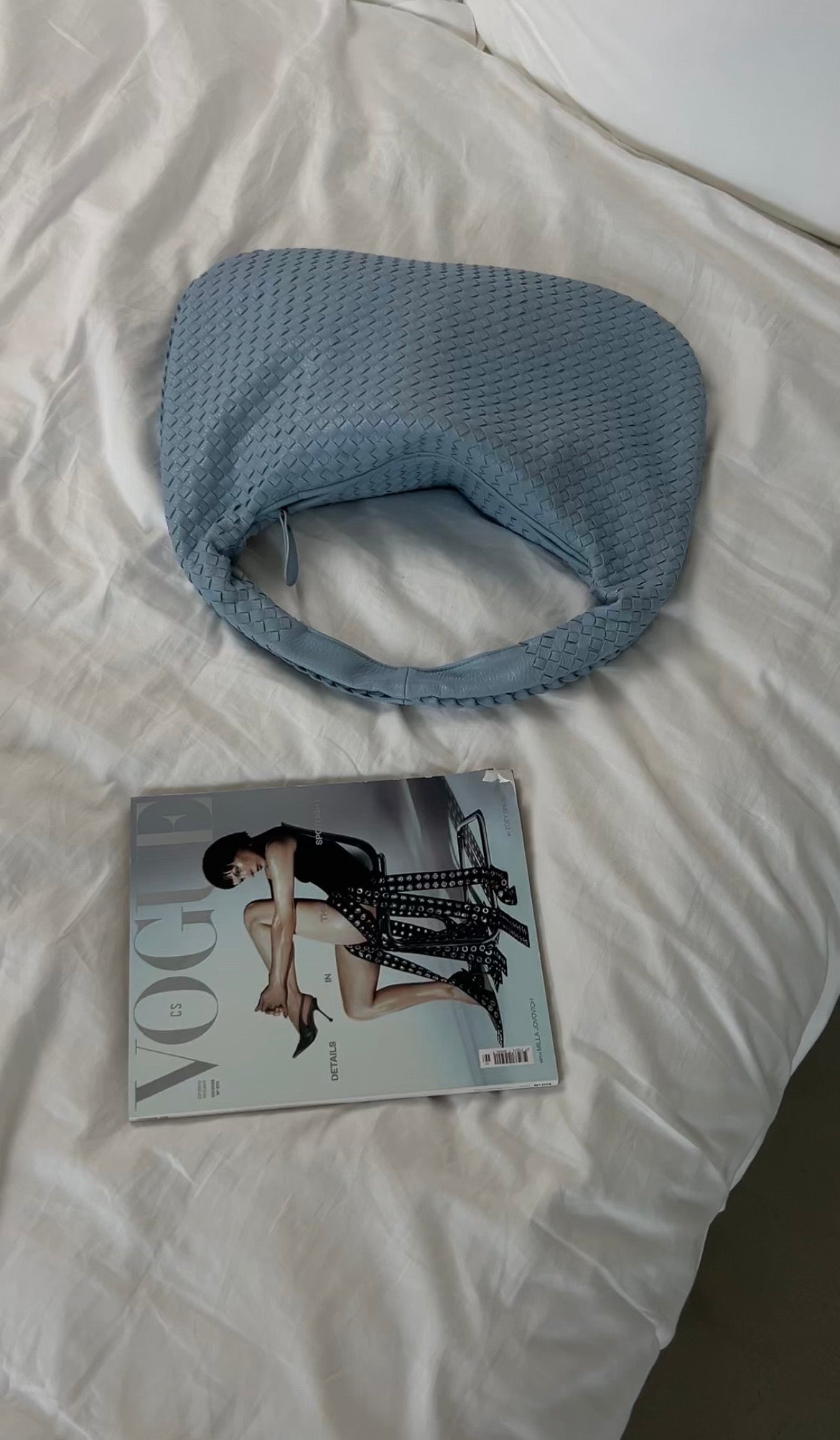 Blue textured bag and Vogue magazine on a white surface