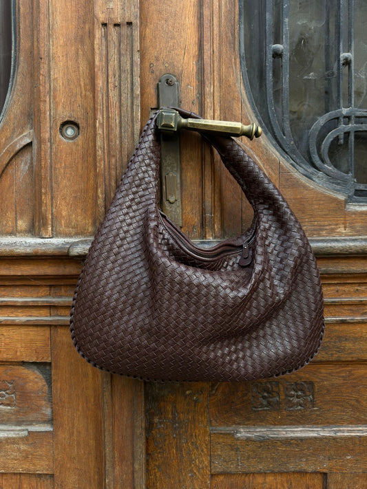 Brown woven handbag hanging on a wooden door with glass panels