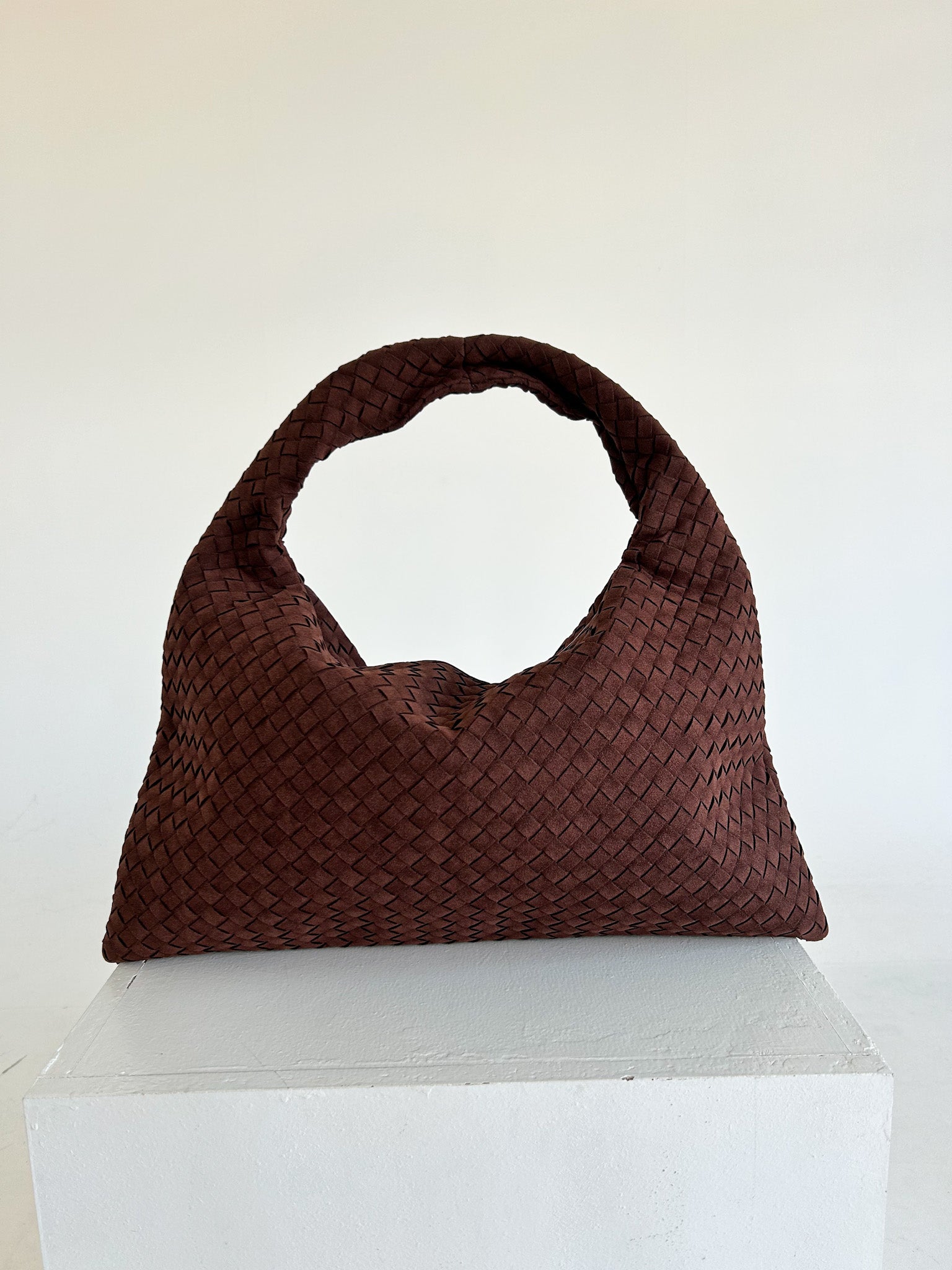Brown woven handbag on a white pedestal against a white background