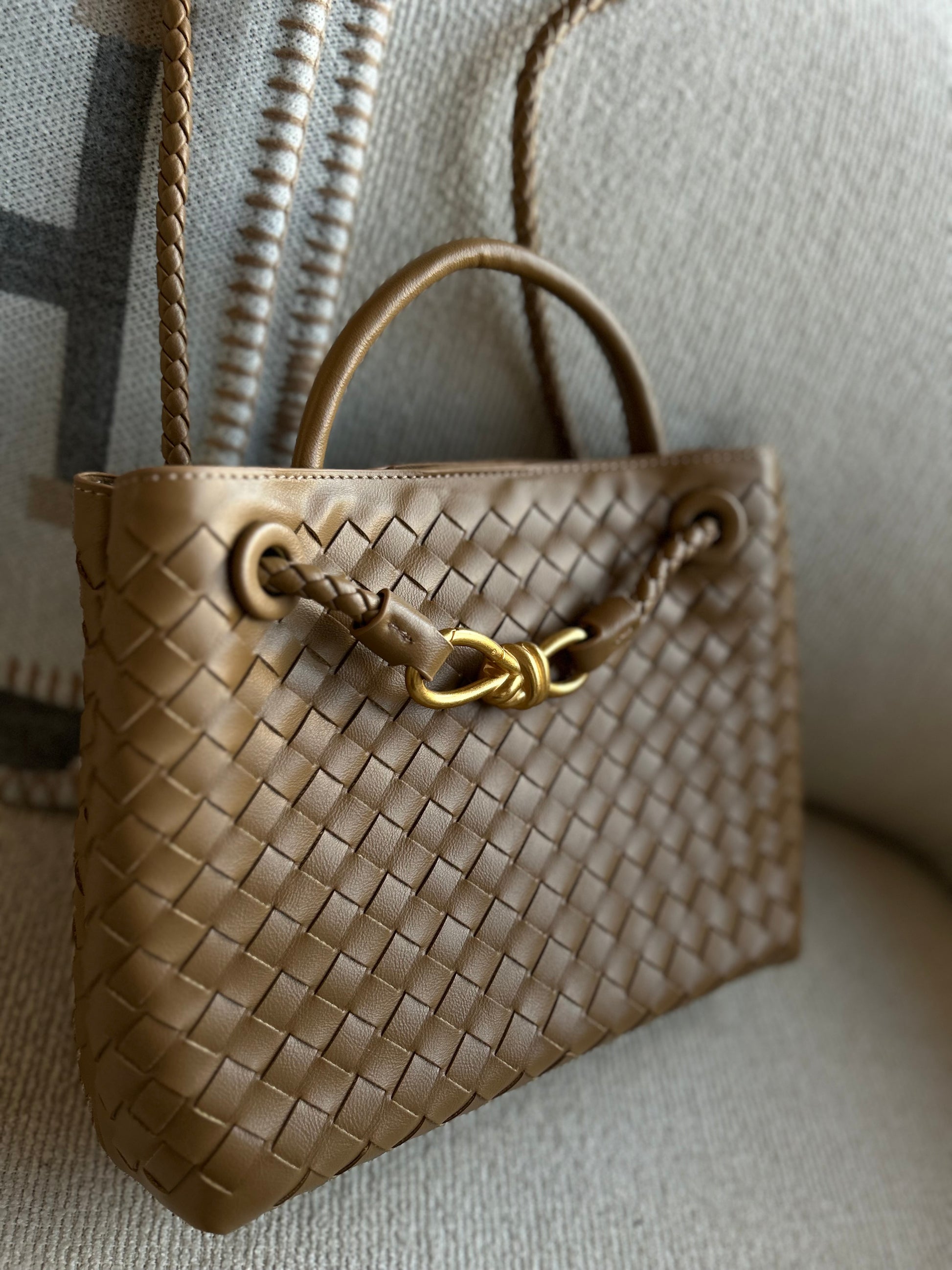 Brown woven handbag with a gold clasp on a textured surface