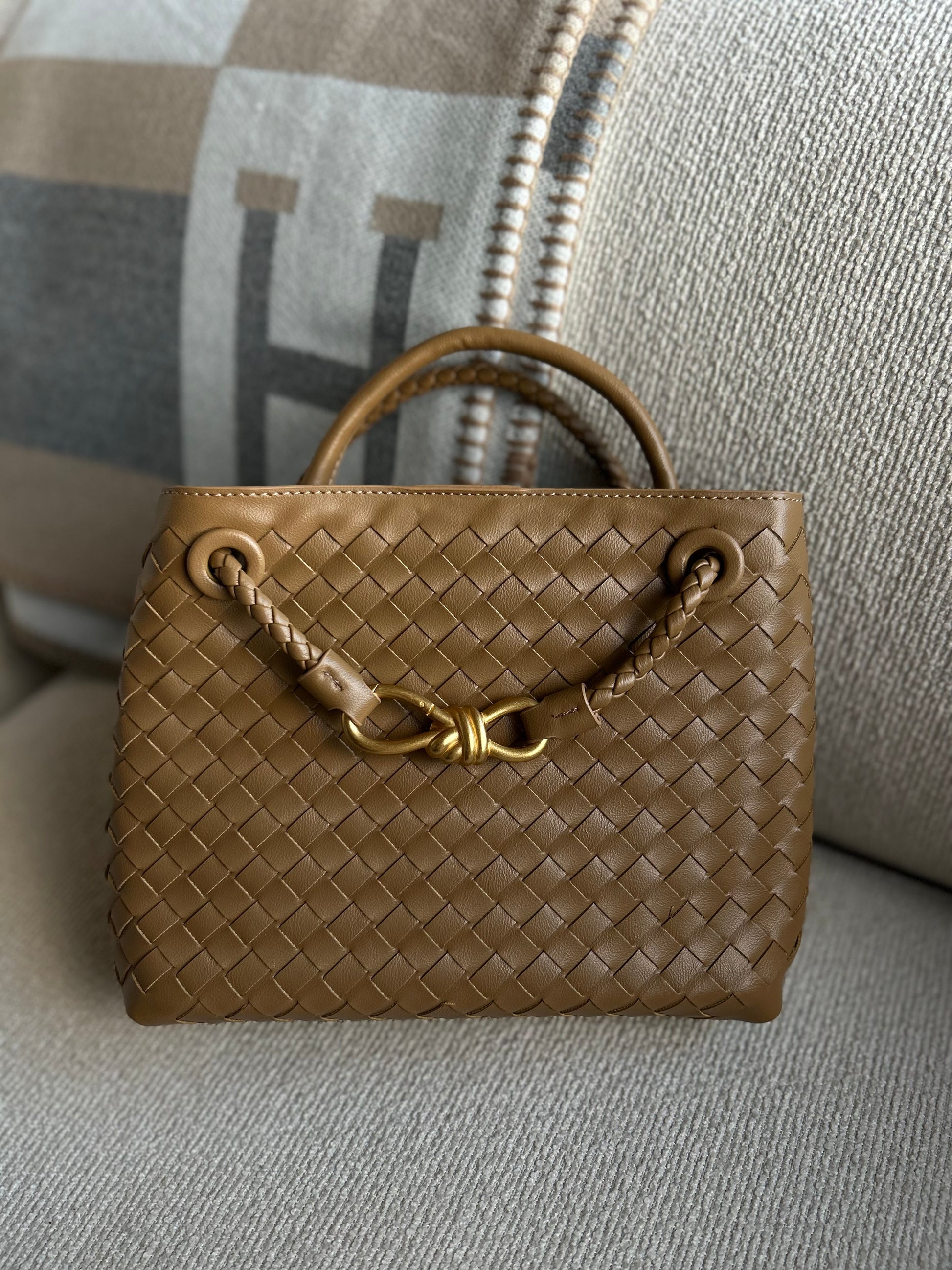Brown woven handbag with gold handle on a gray designer blanket. Elegant woven mini handbag with top handle and detachable strap