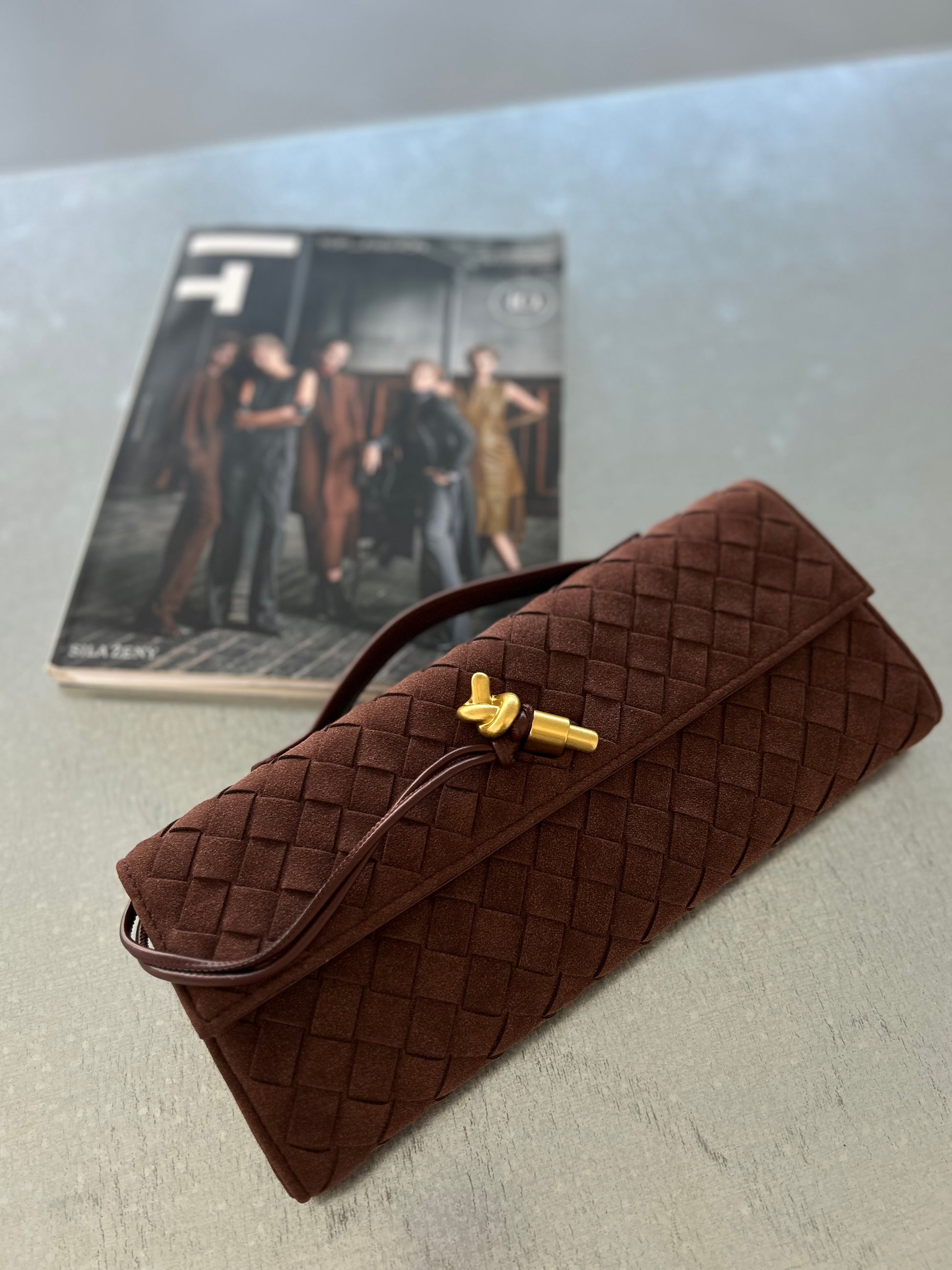 Chocolate brown woven clutch featuring a gold pin closure and detachable strap