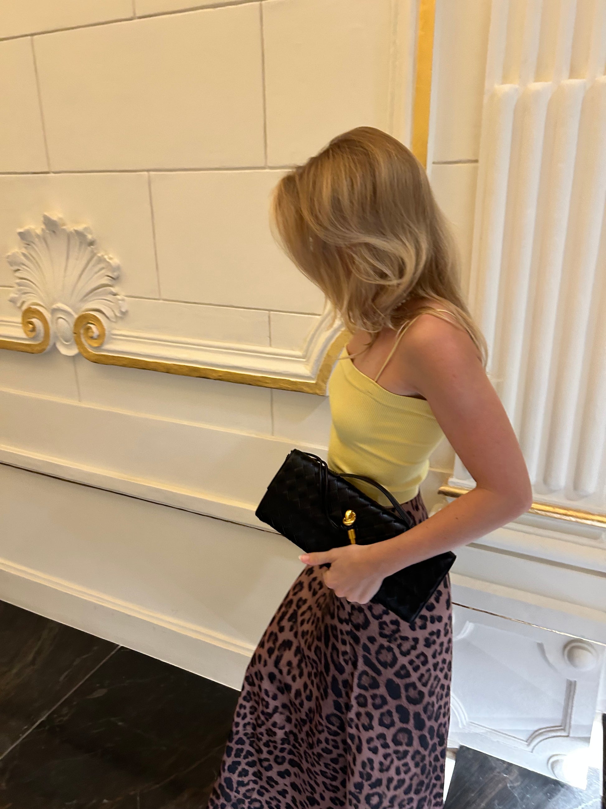 woman in a yellow tank top and leopard print maxi skirt holding a designer inspired black woven clutch with gold pin detail which is suitable for every occasion especially elegant black tie events.  pattybofficial Czech luxury handbags brand