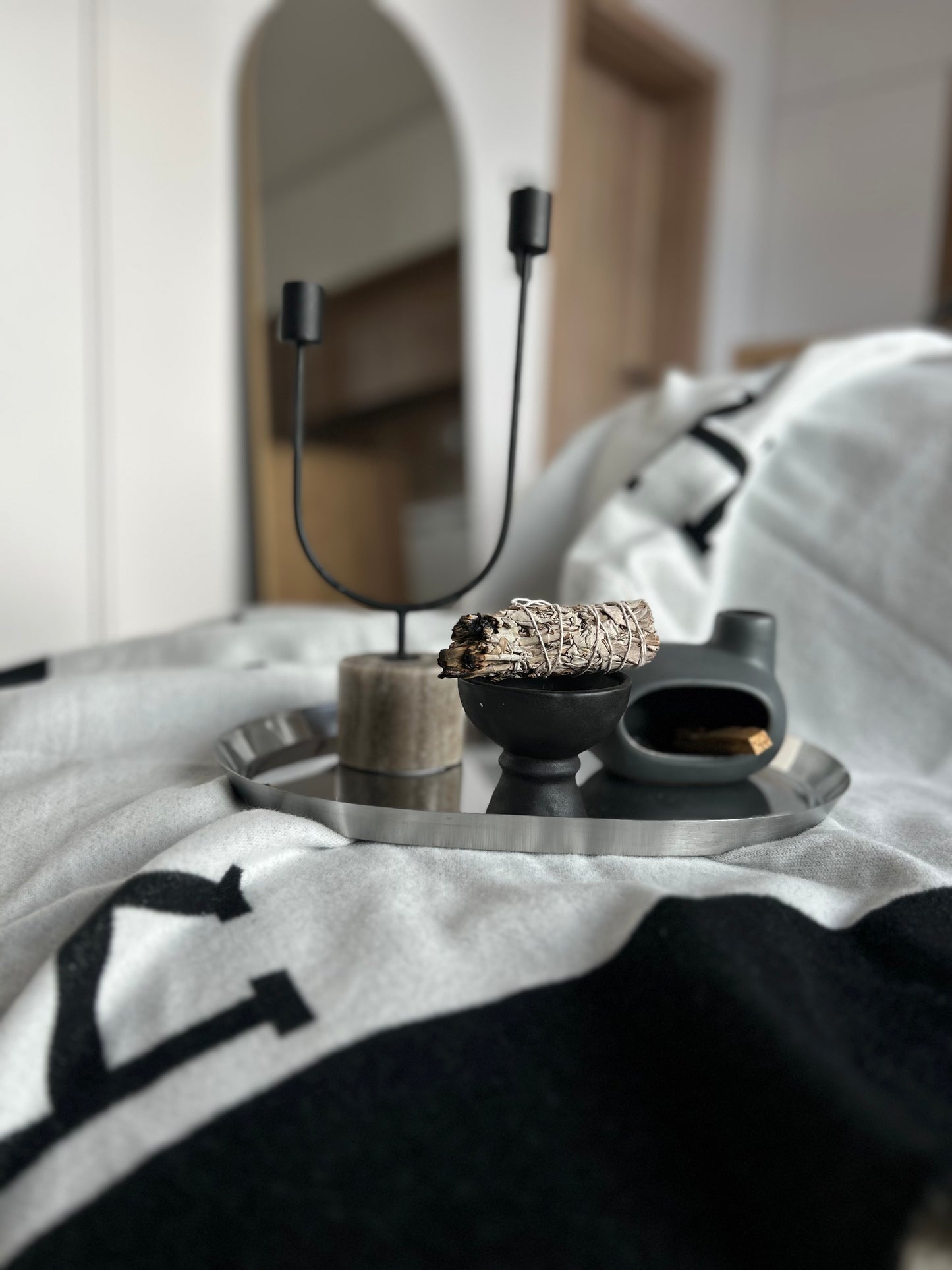 Tray with decorative items on a bed in a bedroom setting. Cozy minimalist living room with black white throw blanket and neutral tones