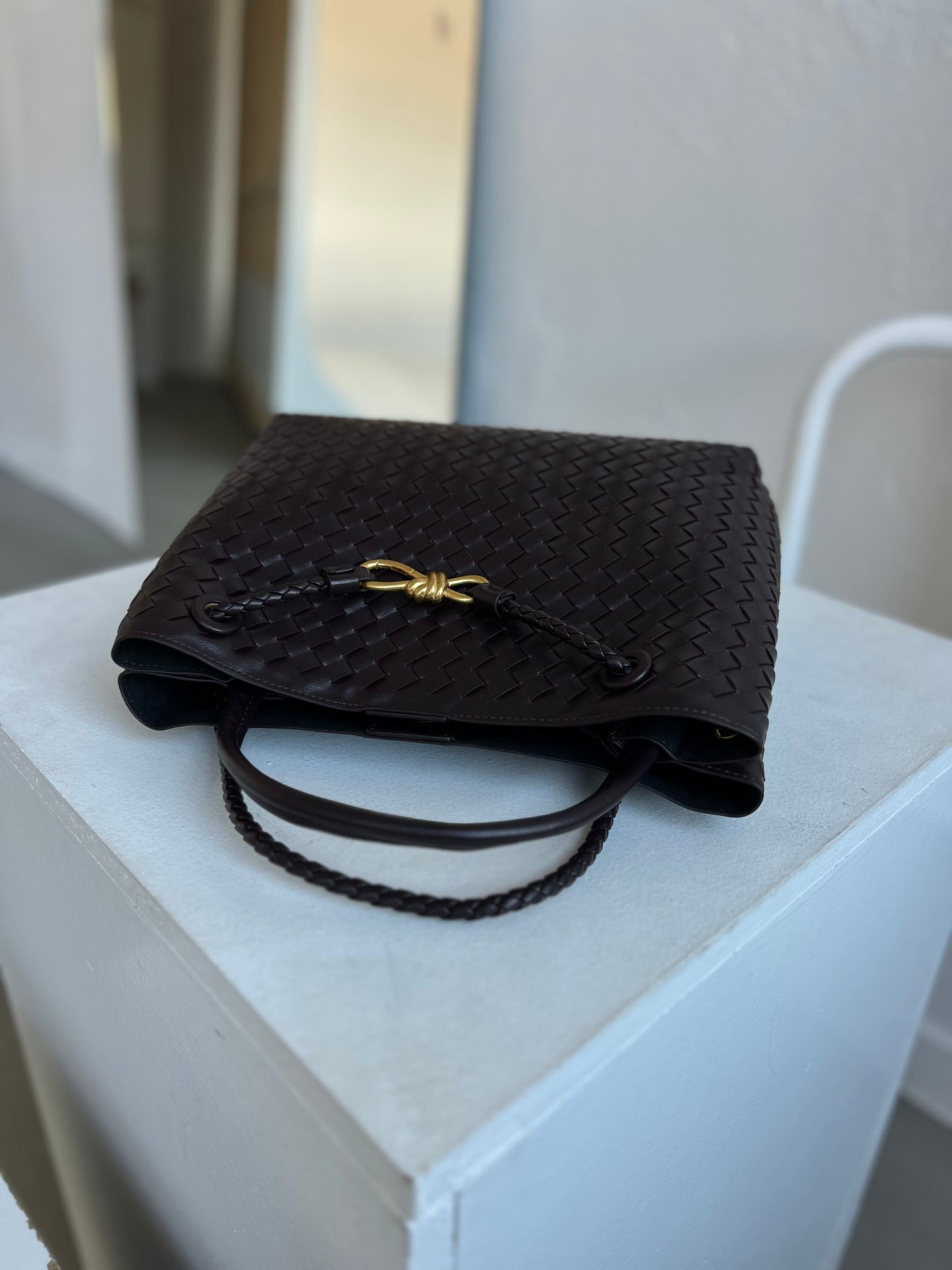 Dark brown vegan leather textured handbag with a gold clasp on a white surface