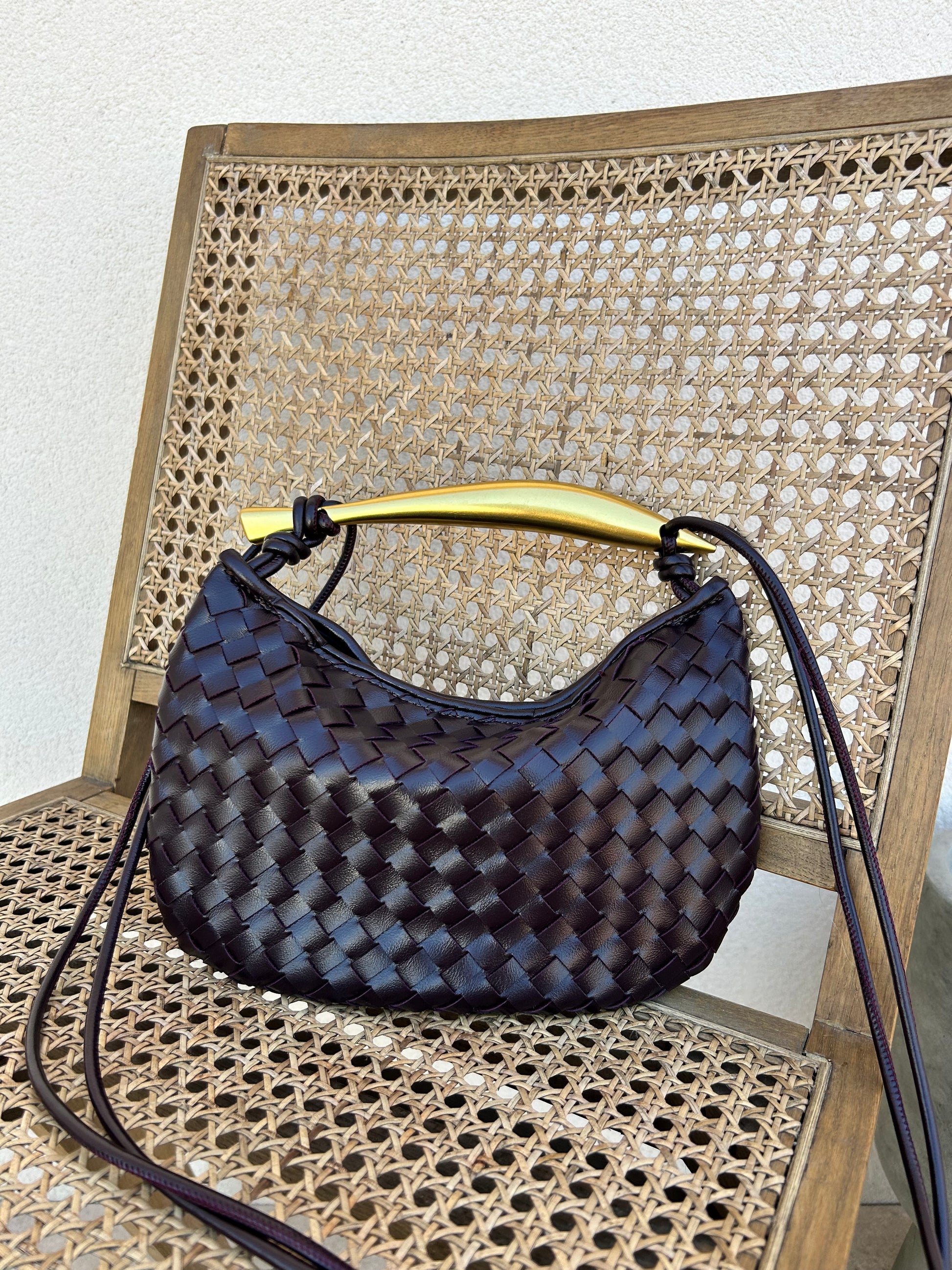 Deep burgundy vegan leather clutch with gold handle on chair