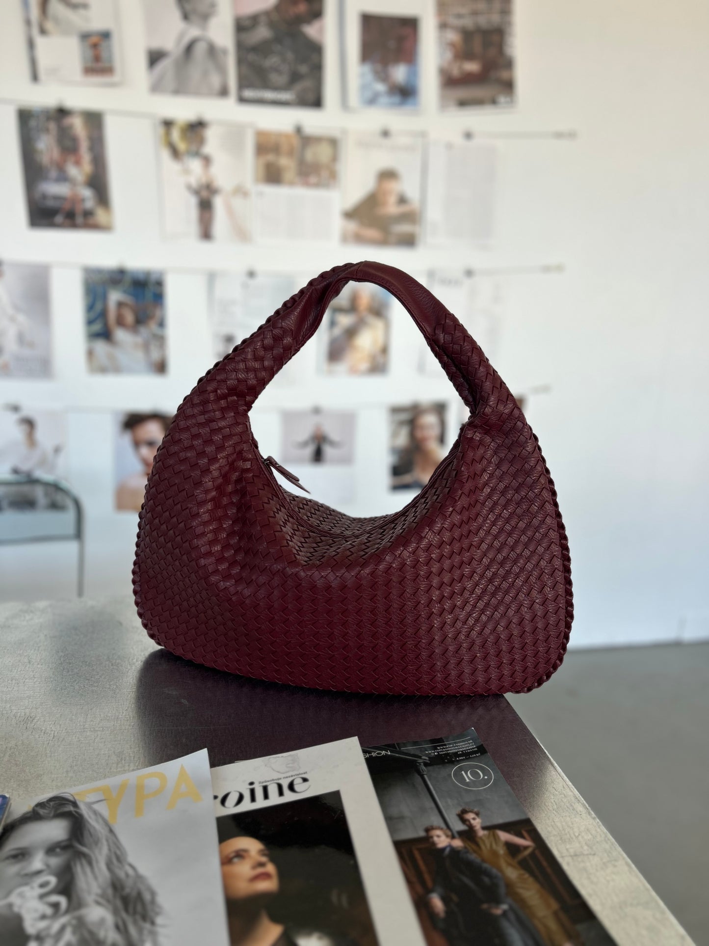 Sleek and Sophisticated Burgundy Woven Purse for Everyday Wear placed on a table with fashion magazines and fashion vision board in the background Braided Texture Handbag Ideal for Business Women Travel Bag with Zip Closure