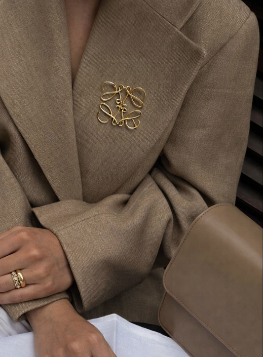 Gold monogram brooch on beige blazer in quiet luxury old money style