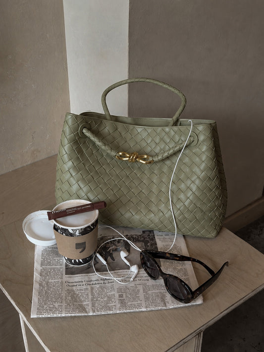 Green handbag on a table with a newspaper, sunglasses, and a cup.