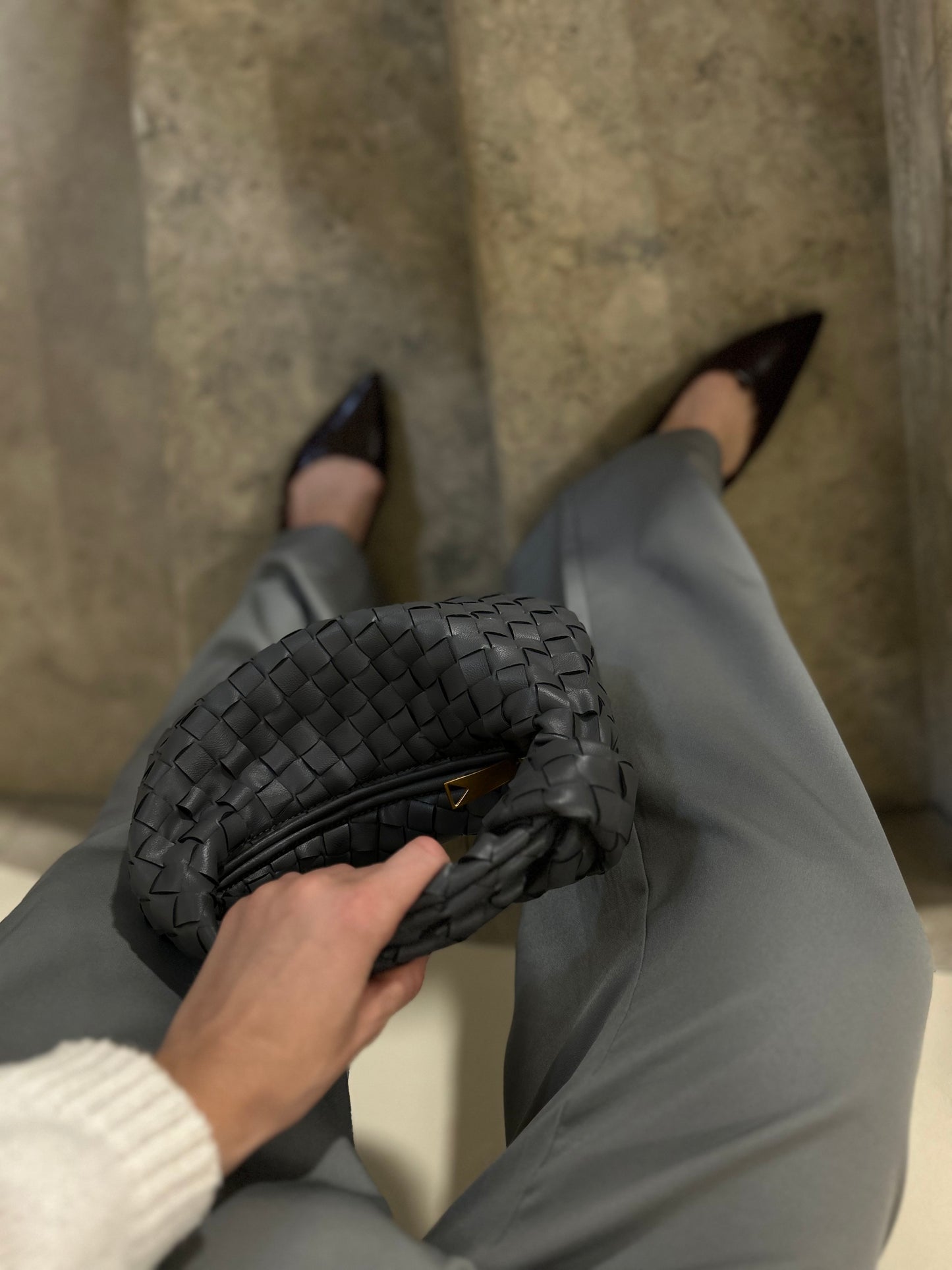 Grey woven clutch bag styled with tailored trousers and heels