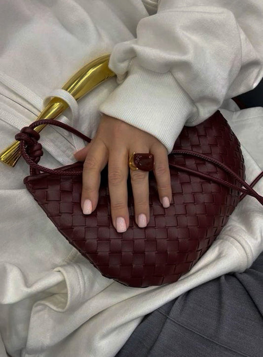 Hand holding a woven burgundy vegan leather bag with a blurred background
