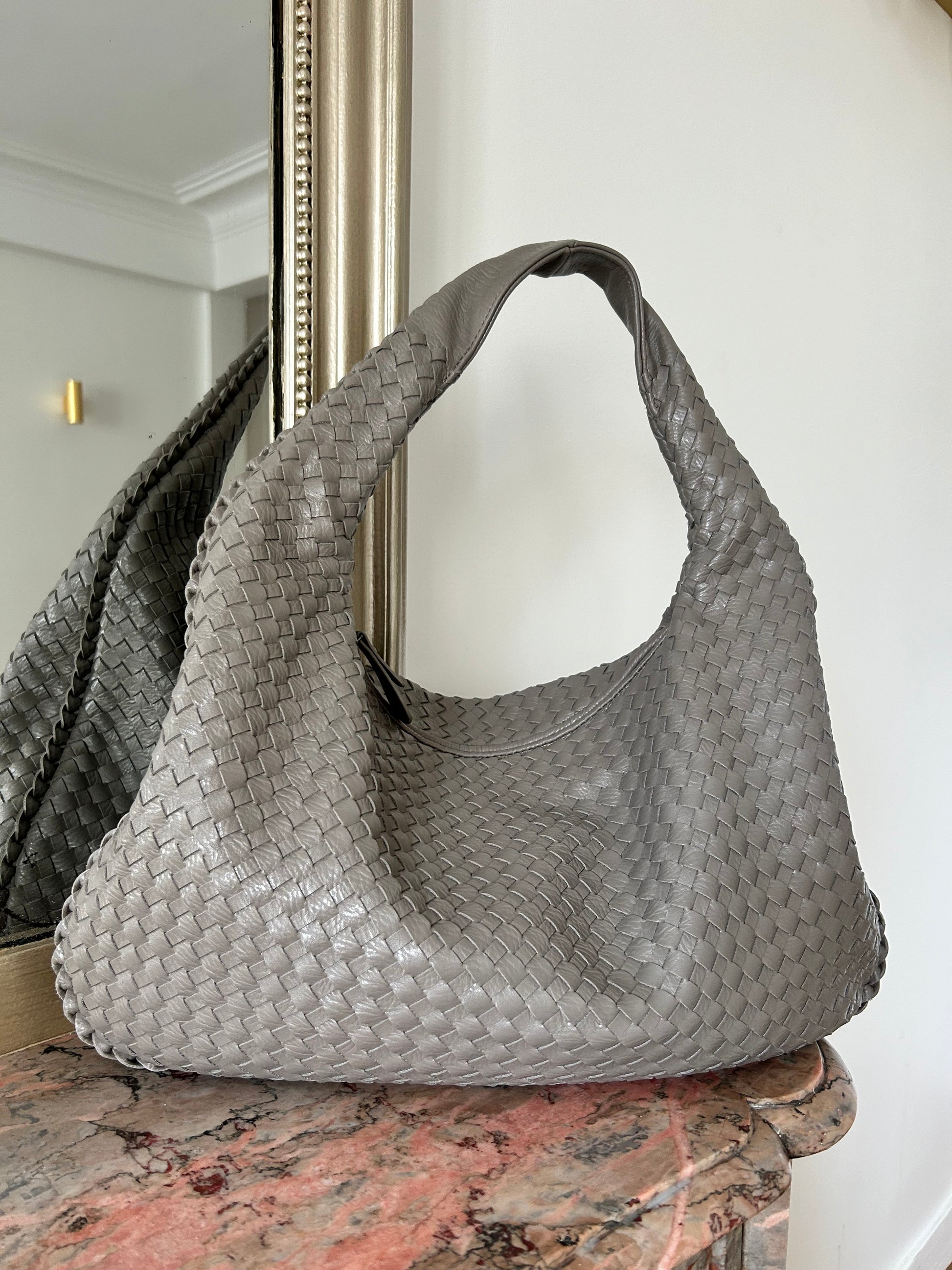 Chic Influencer Hobo Bag in grey colour Trendy Dark Grey Handbag with zip fastening Woven Dumpling Oversized Purse Women Small Vegan Leather Handbag Cute Summer Bag Oversized Style inspired by designer shoulder handbag which is placed by a mirror to create aesthetic look