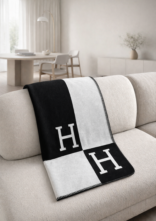 Black and white patterned blanket with 'H' on a beige sofa in a modern living room. Minimalist black and white throw blanket draped over beige sofa in modern living room