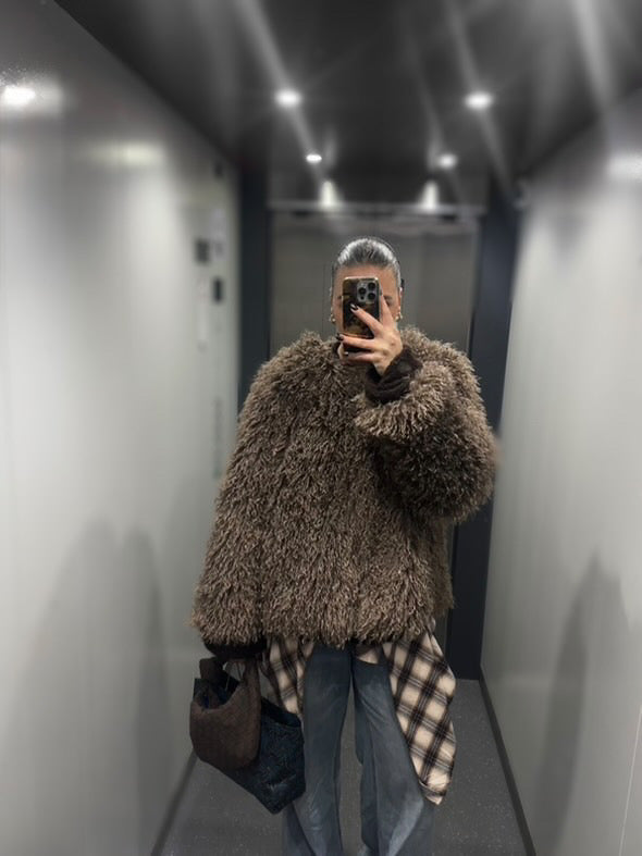 Minimalist chocolate brown clutch bag held in hand by a dark haired woman wearing a fur coat.