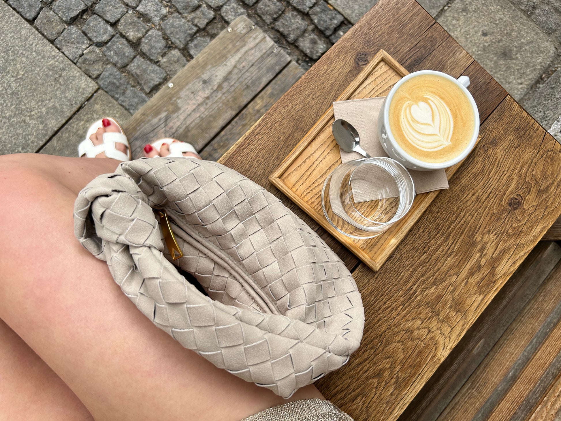 Neutral suede clutch styled with beige outfit placed next to a coffee