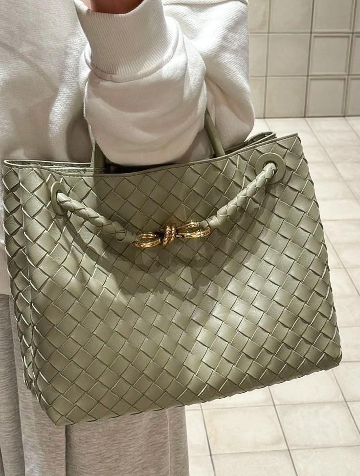 Person holding a green woven handbag with a gold clasp on a tiled floor.