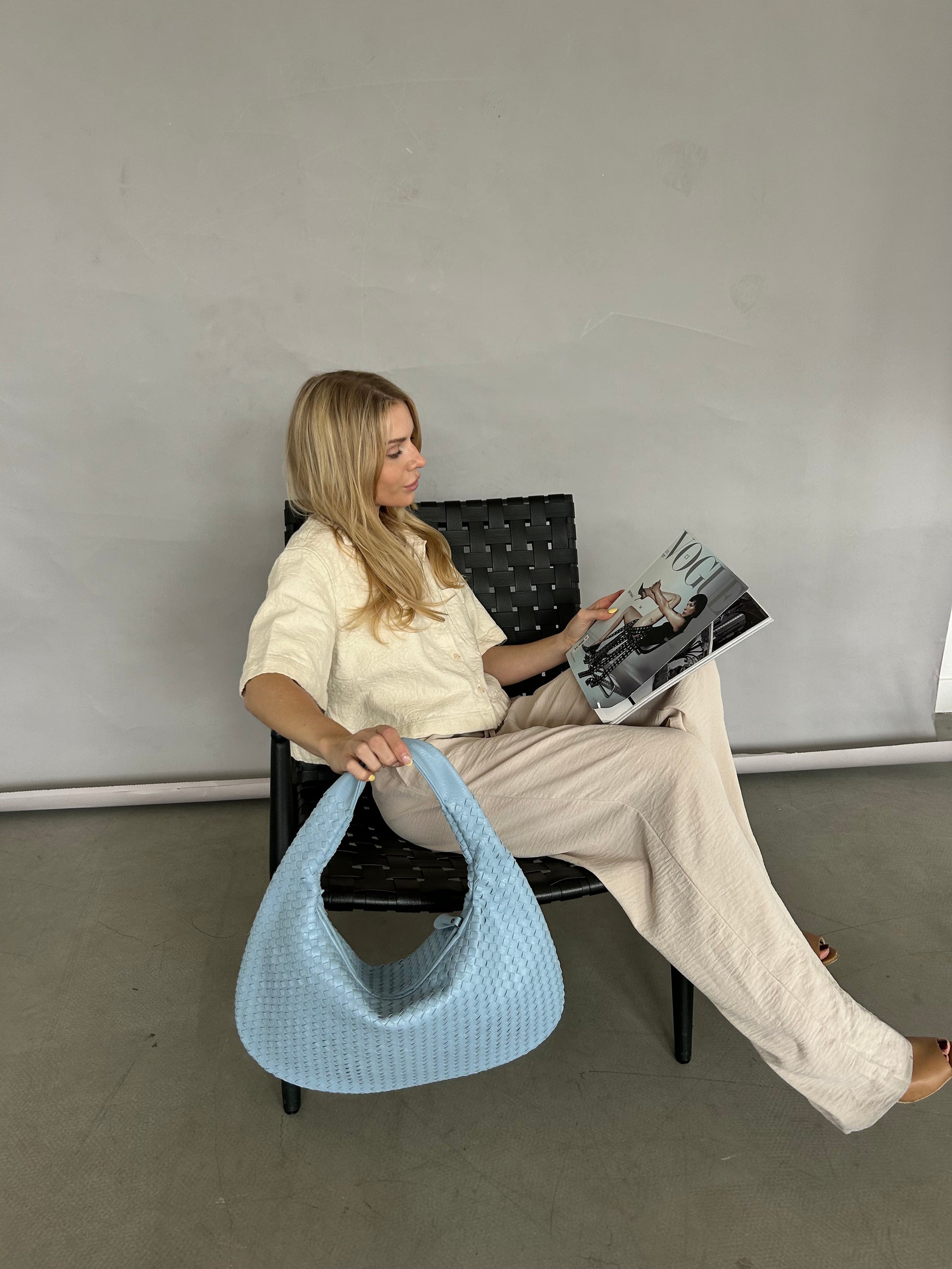 Person sitting on a chair holding a book with a blue bag beside them against a plain background