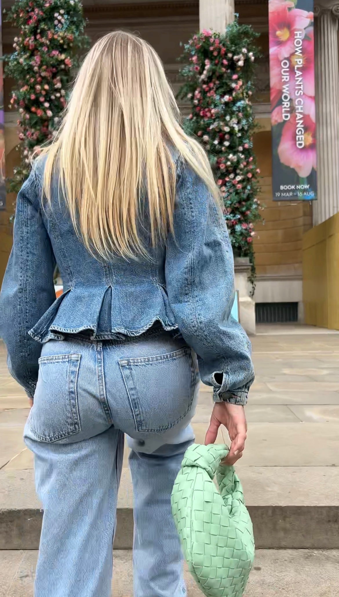 Person wearing a denim outfit with a peplum top and jeans, holding a green handbag.
