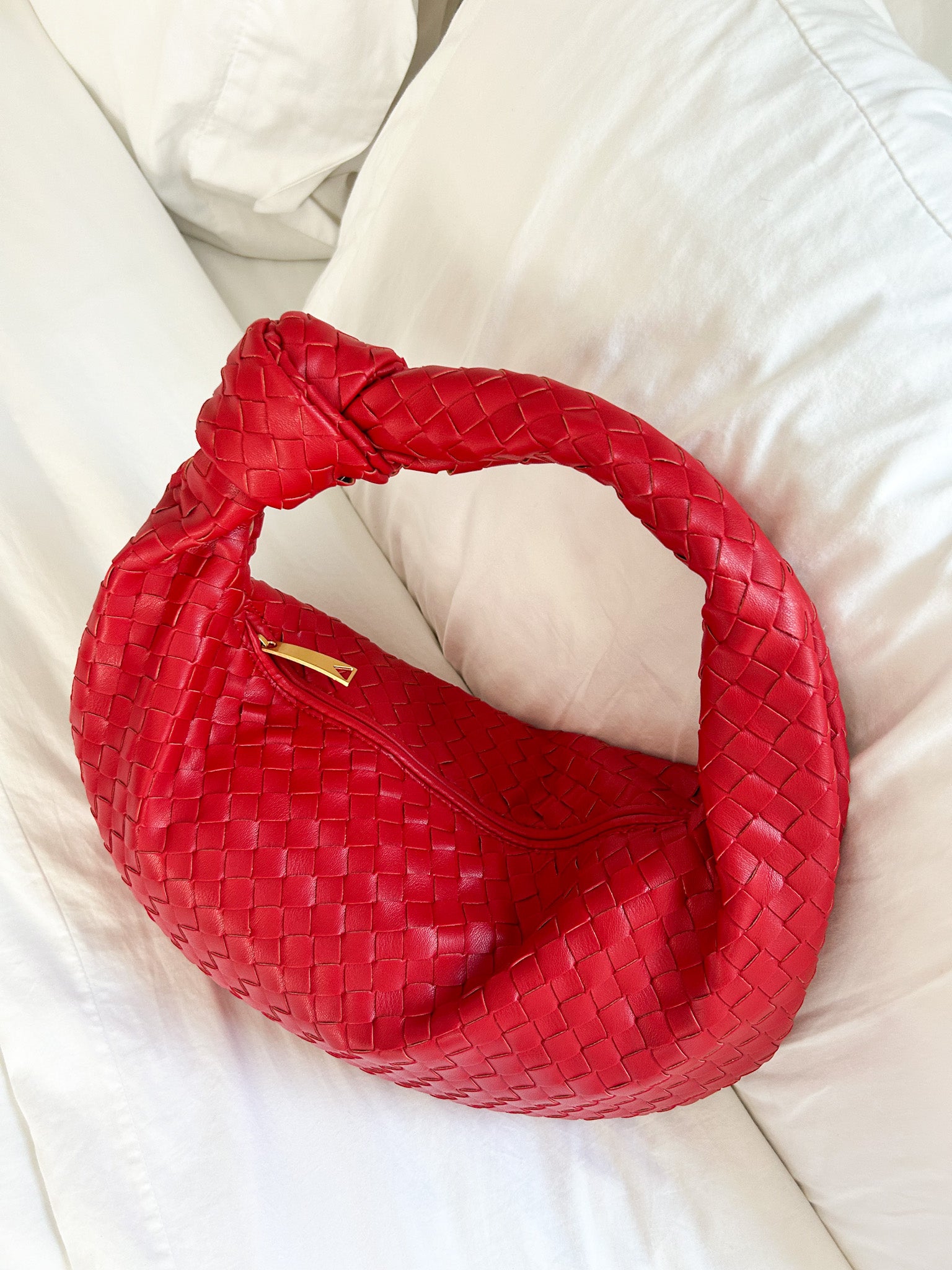 Red woven hobo shoulder bag with luxury-inspired design styled indoors on a bed.