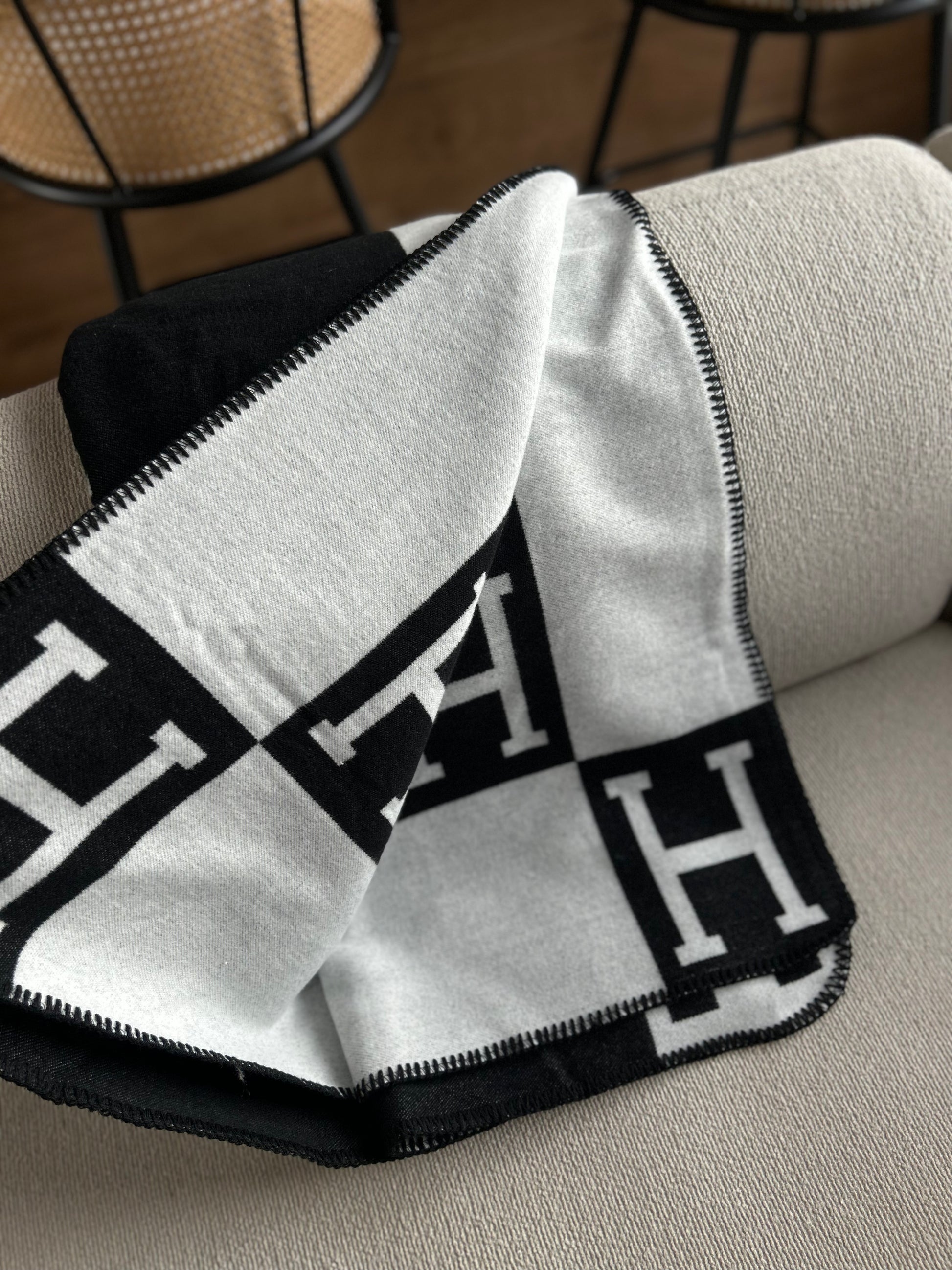 Black and white patterned blanket draped over a chair with a blurred background. Soft knit black and white blanket folded on chair minimalist interior styling