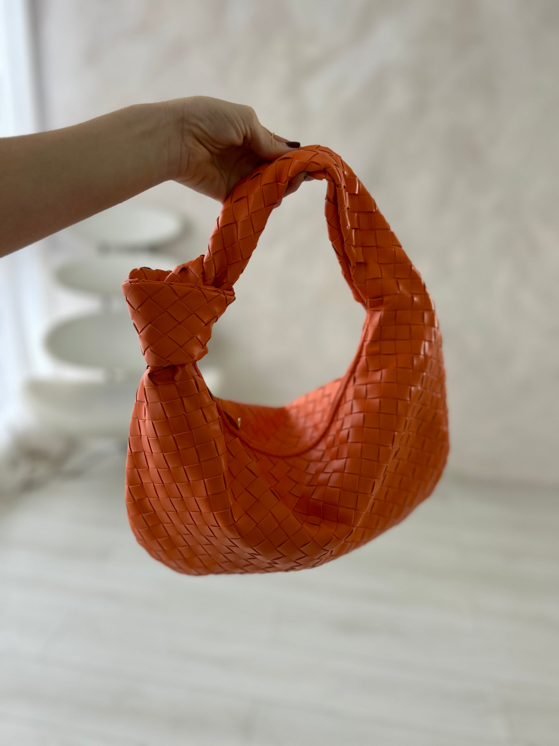 Bold orange intrecciato-style leather bag with a knotted handle and geometric zip, displayed in a luxury setting. Spacious 40x30 silhouette ideal for everyday elevated looks.