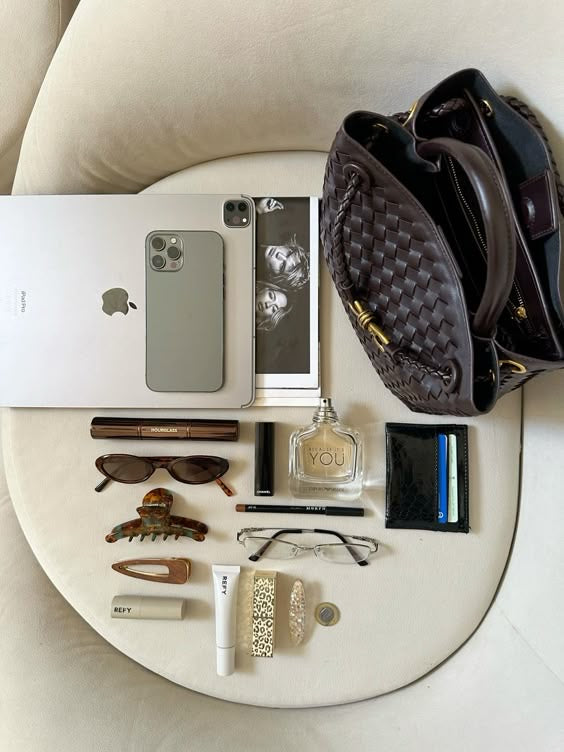 Collection of personal items including a phone, sunglasses, perfume, and wallet on a white surface.Structured brown woven handbag with gold hardware photographed indoors for product styling