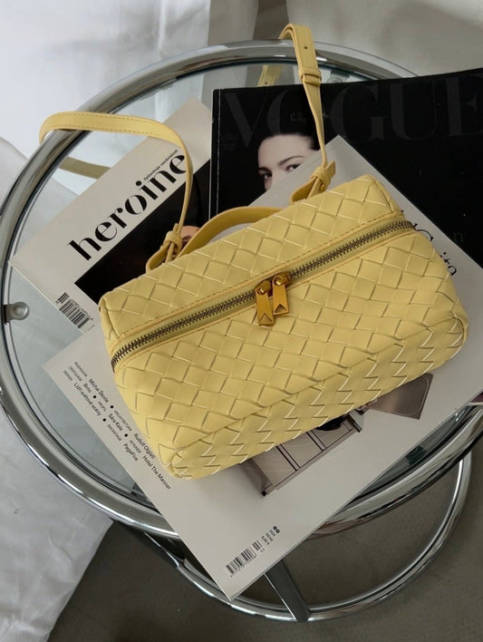 Yellow woven handbag on a glass table with a magazine underneath, next to a pair of slippers.