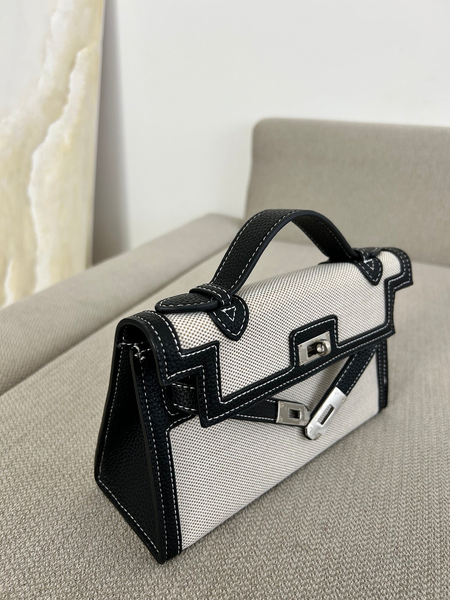 Crafted from premium textured canvas with bold black leather-look trim and contrast stitching, this beauty means business. The silver-tone hardware and unique dual-strap illusion detail add a high-fashion edge, while the structured silhouette screams polished perfection. 