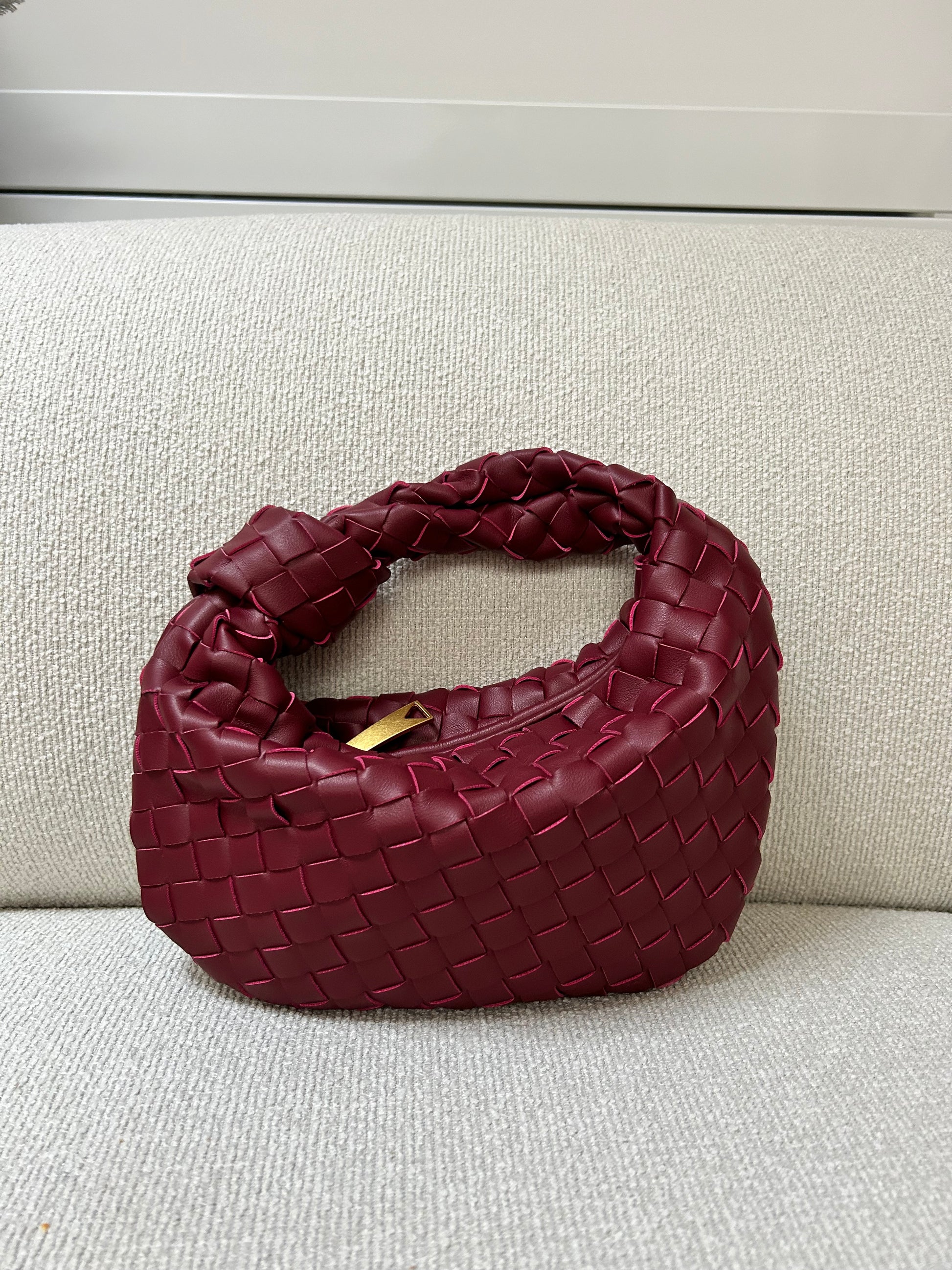 burgundy woven handbag placed on a cream sofa