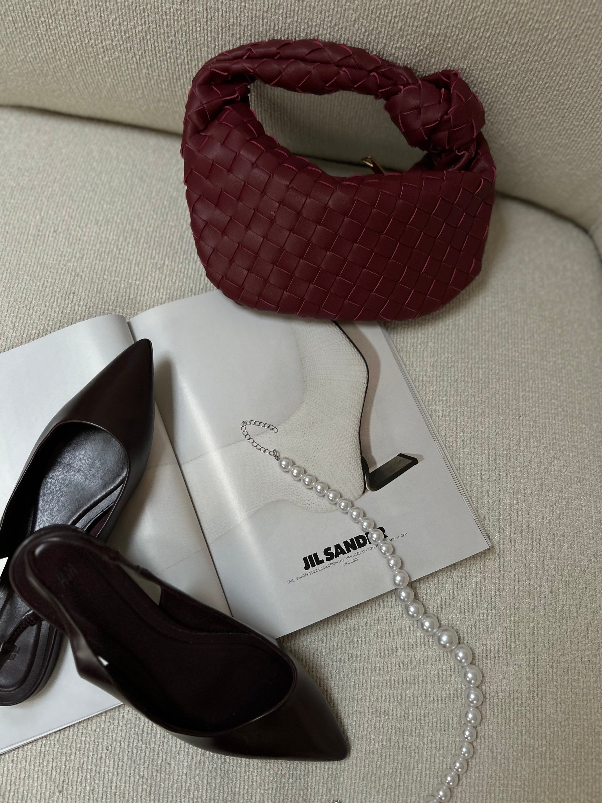 deep merlot woven clutch bag on neutral background with luxury accessories minimalist aesthetic