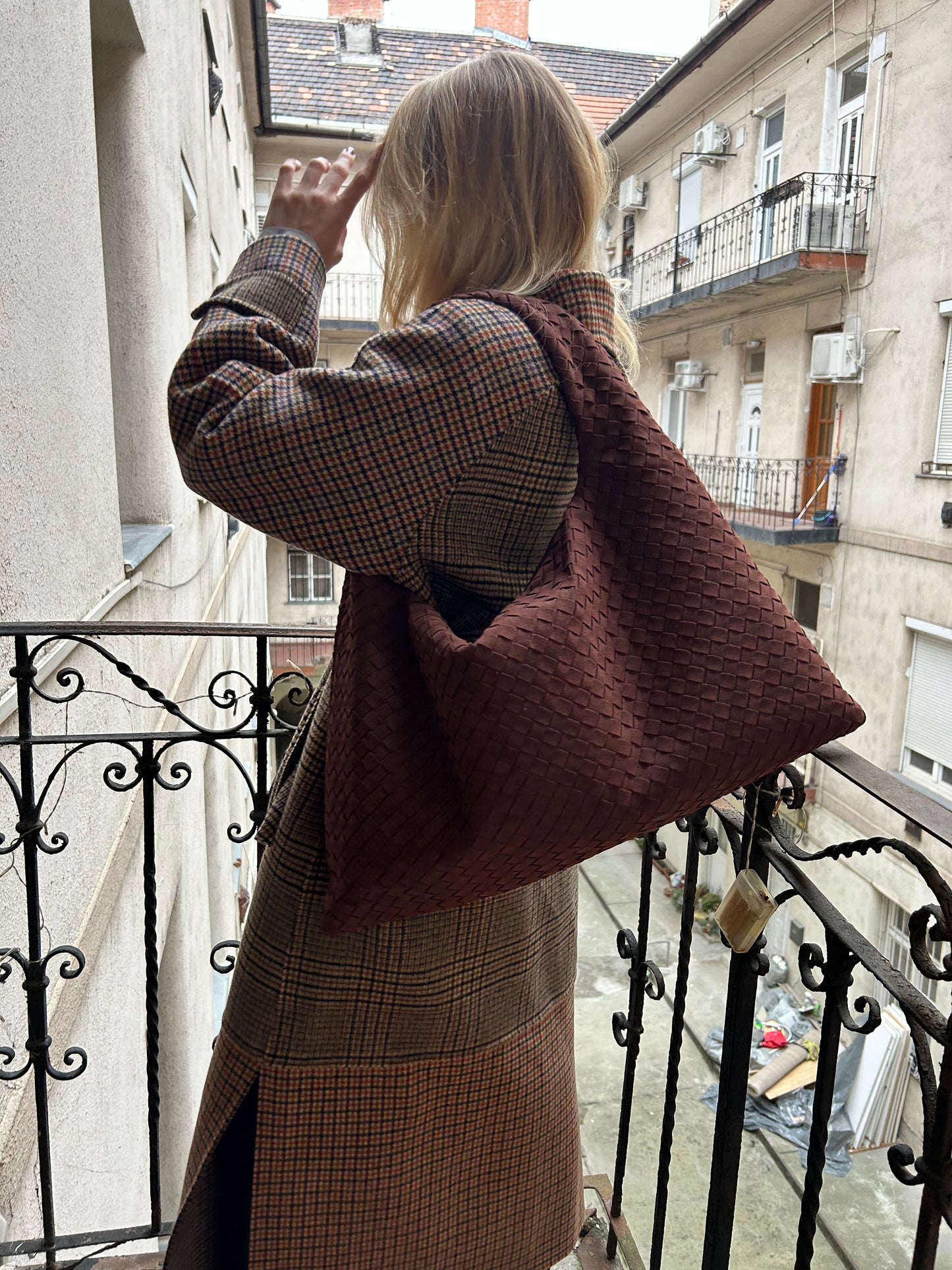 blonde woman in Budapest Hungary standing on a balcony in winter wearing warm winter coat with luxury hobo suede shoulder bag from vegan leather the bag is in stylish chocolate brown colour inspired by famous designer practical everyday purse for her