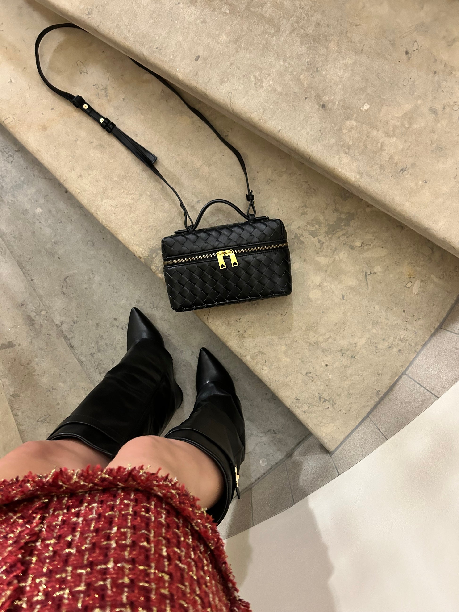 Black braided crossbody clutch placed neatly on stairs, highlighting its elegant woven texture and compact design. This versatile accessory is perfect for everyday use or special occasions, combining functionality with a chic, sophisticated style