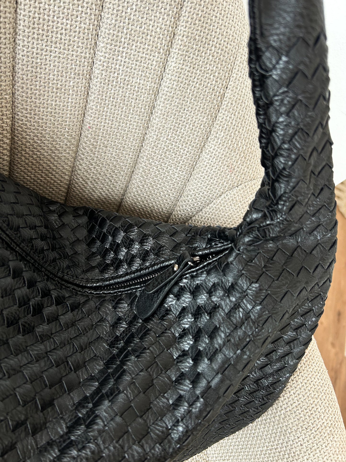 Modern black woven handbag resting on a staircase, featuring minimalist design, soft strap, and triangle zipper—stylish and functional for work or travel. Spacious black vegan leather bag with an elegant woven texture and structured silhouette. Perfect as a trendy, cruelty-free work bag or versatile everyday tote.