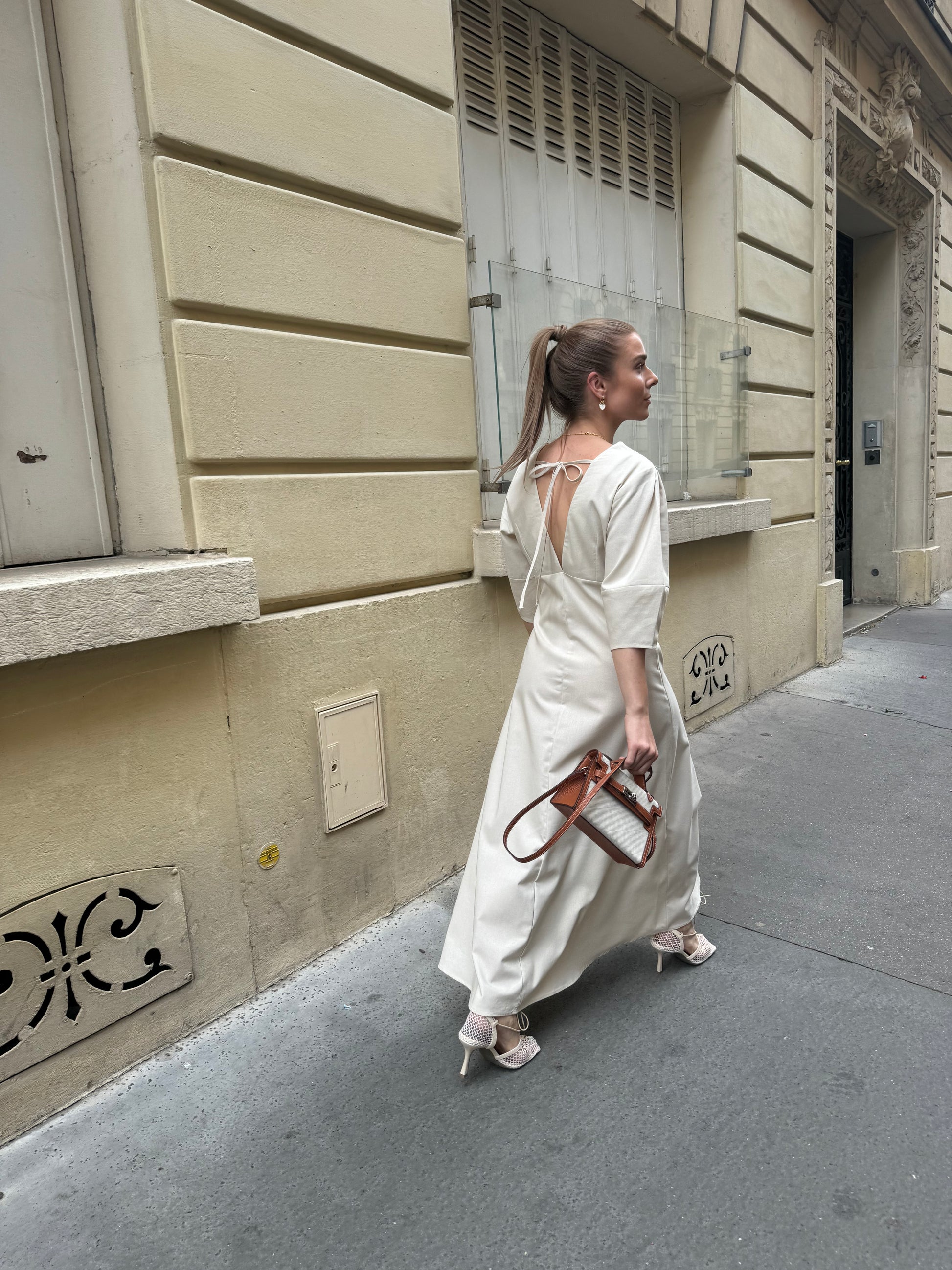 a woman in a A-line linen dress walking the streets of Paris, wearing a monochrome crossbody handbag. This purse is of brown and beige colour, made from canvas.
