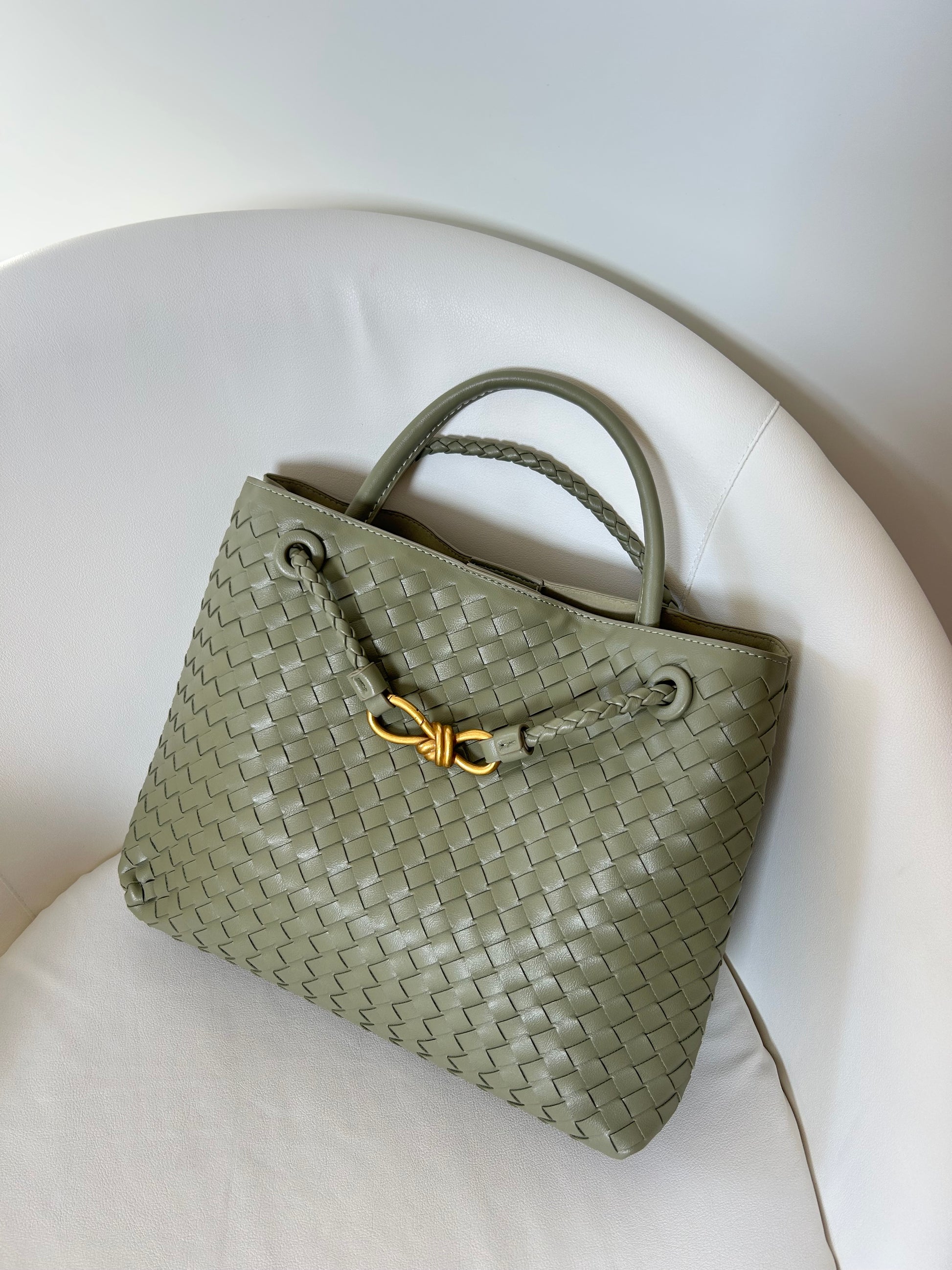 sage Green woven handbag with a gold clasp on a white cushion