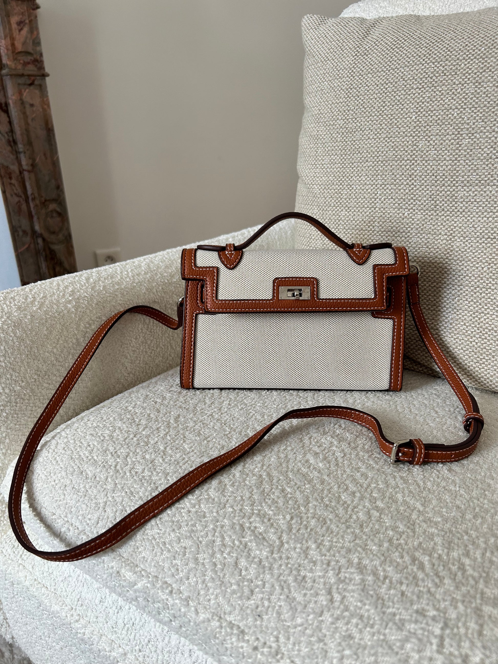 Crafted from premium textured canvas with bold black leather-look trim and contrast stitching, this beauty means business. The silver-tone hardware and unique dual-strap illusion detail add a high-fashion edge, while the structured silhouette screams polished perfection. Whether you're heading to a coffee meeting or jet-setting to your next luxury escape, this bag always delivers main-character energy.
