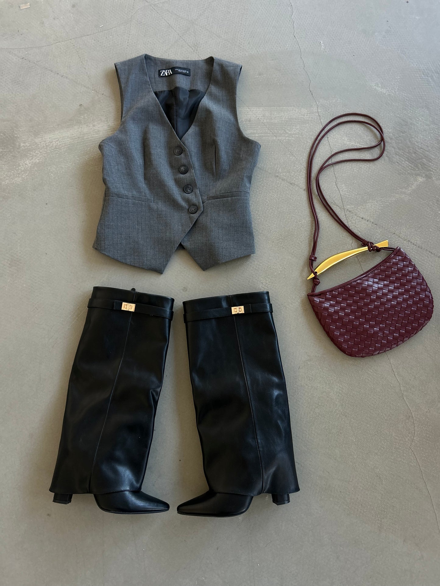 outfir inspiration for spring 2025 consisting of a woven burgundy purse with gold bar detail, black leather boots and grey waistcoat